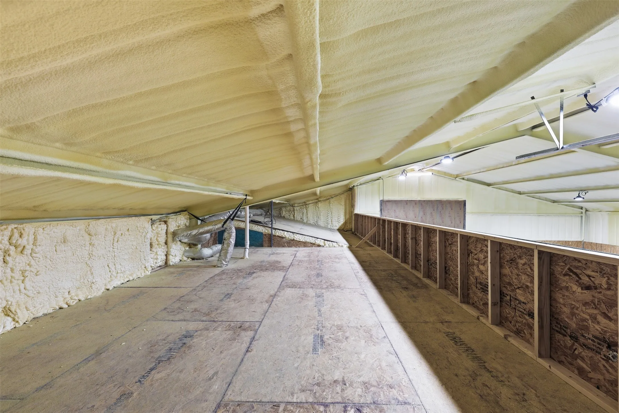 Vaulted ceiling with spray foam insulation, exposed wood-finish flooring, and structural wood railing