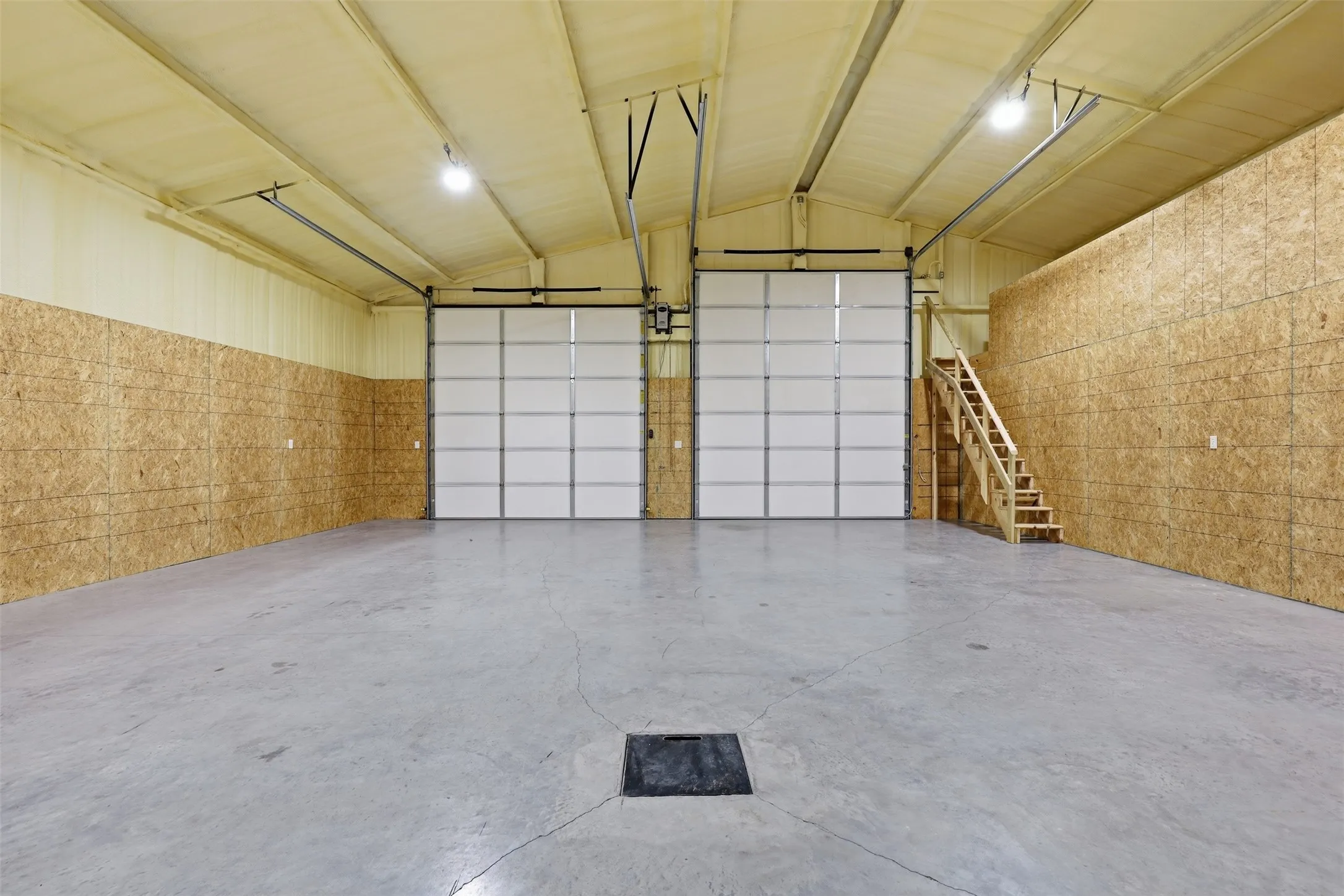 Spacious interior with concrete flooring, two large roll-up doors, high ceilings, and a built-in wooden staircase