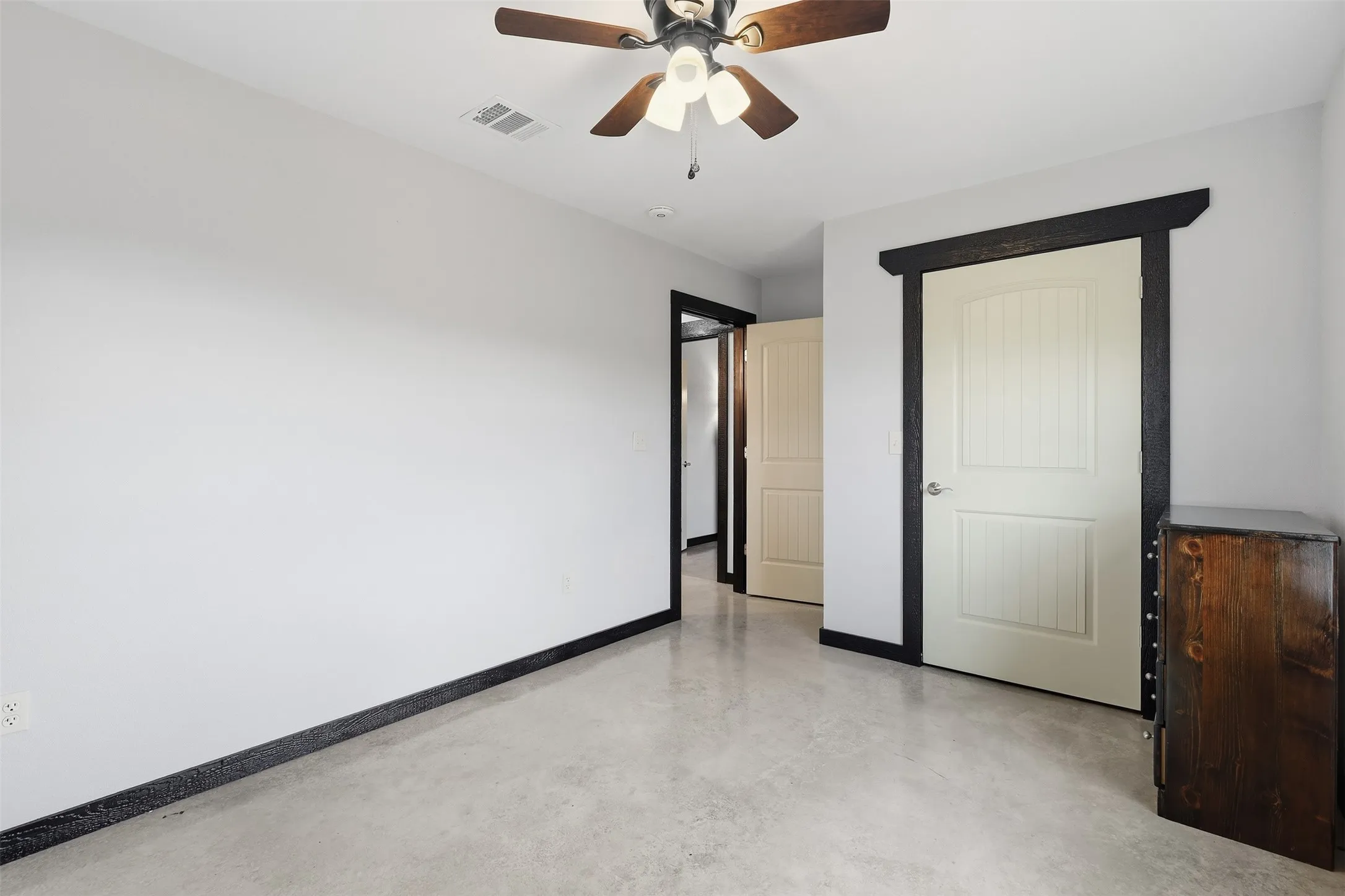 White walls, concrete flooring, wood ceiling fan with light kit, and dark wood trim