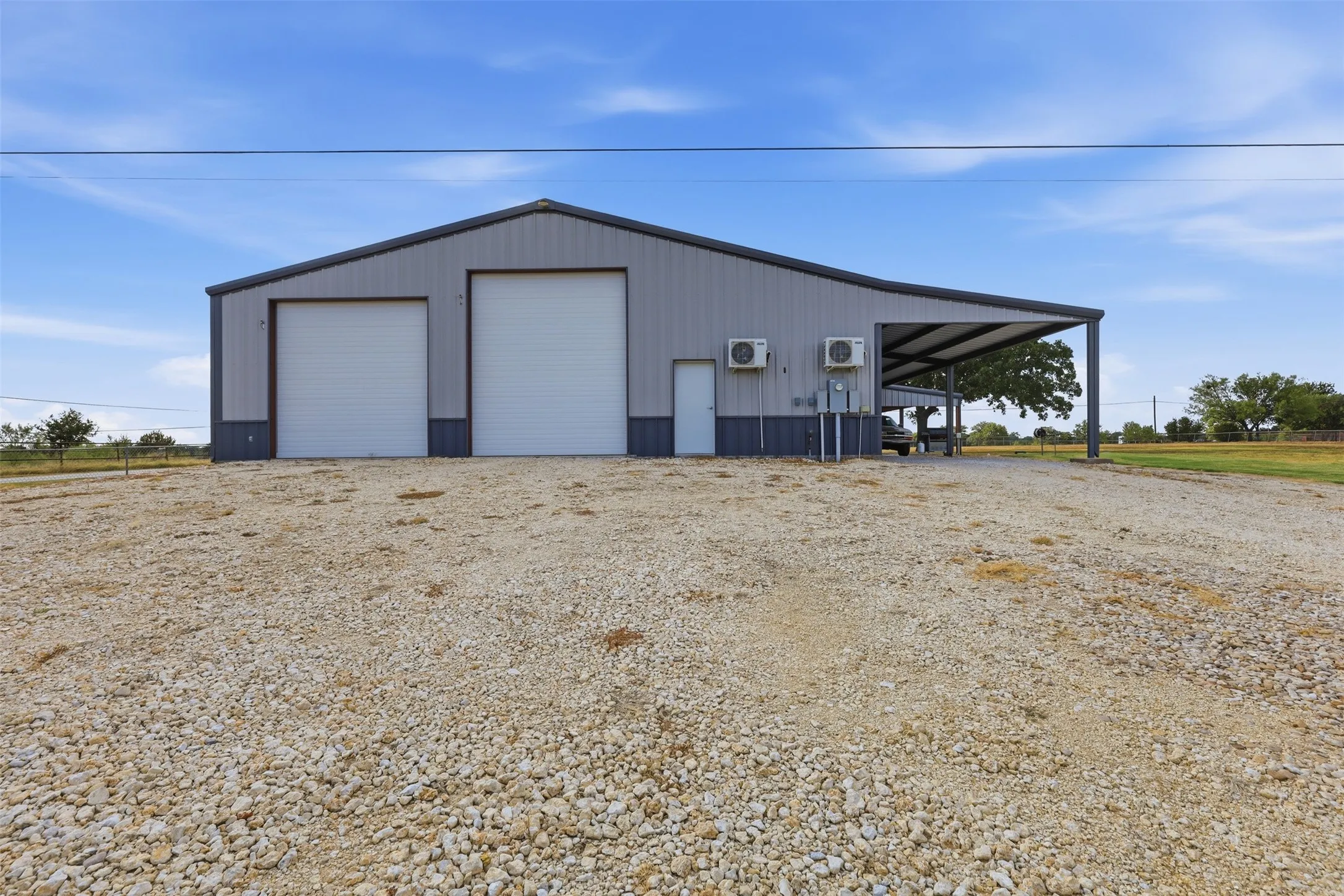 Metal building with two roll-up garage doors, a side entry door, and an attached covered carport