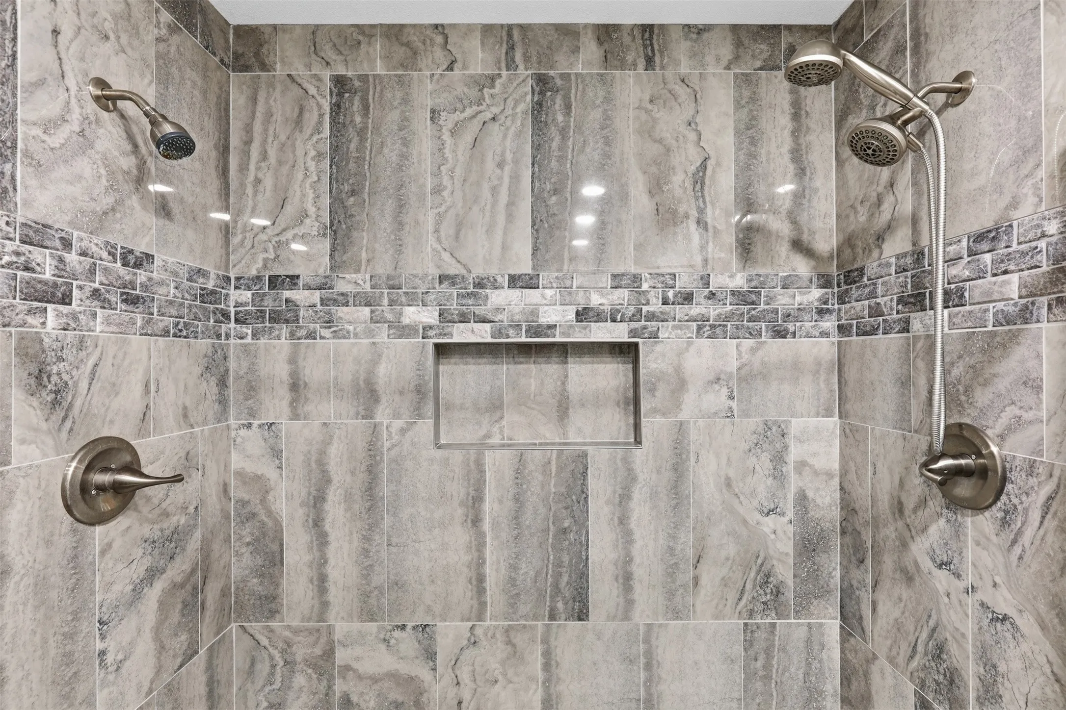 Tiled shower with a mosaic accent band, integrated recessed niche, dual showerheads, and brushed nickel fixtures