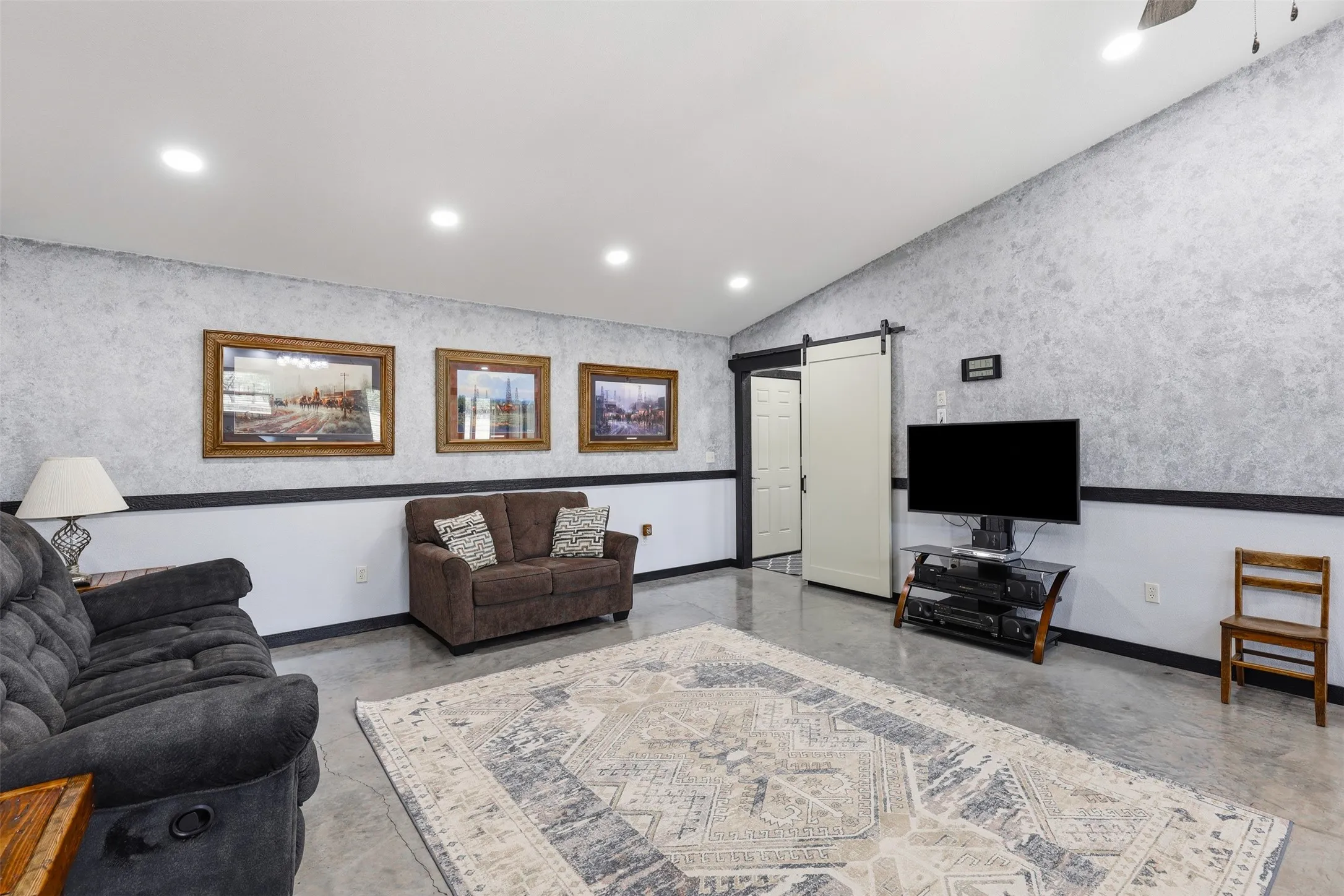 Spacious room featuring a vaulted ceiling with recessed lighting, concrete flooring, and a sliding barn door