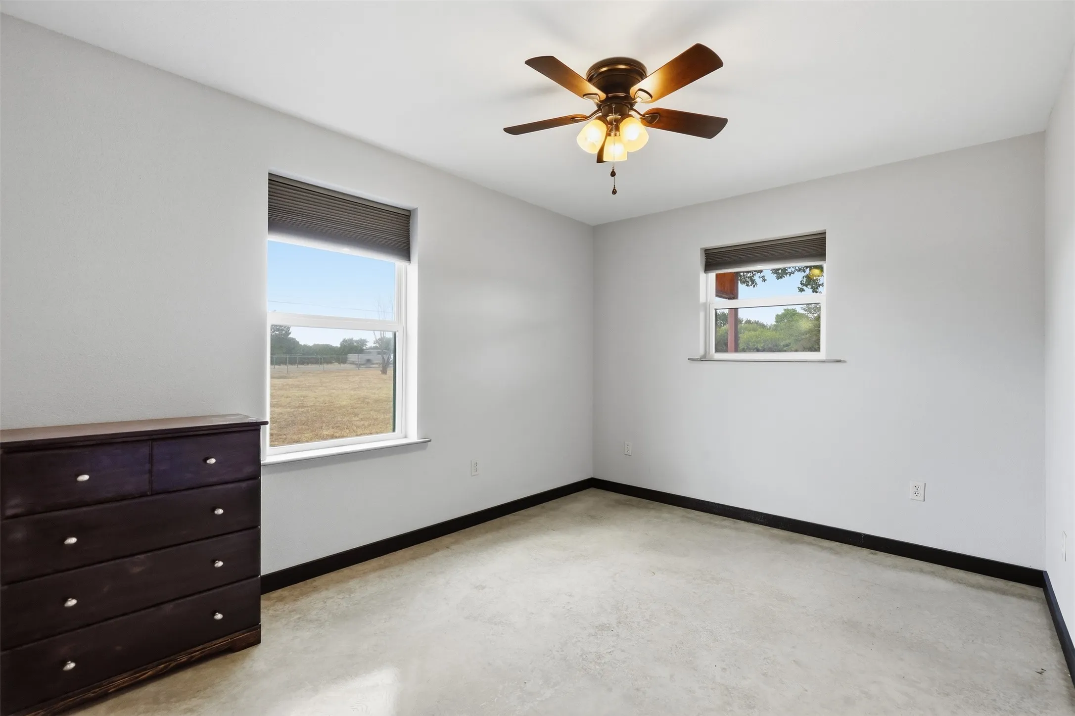 Room featuring two windows with blinds, a ceiling fan with integrated lighting, and polished concrete flooring