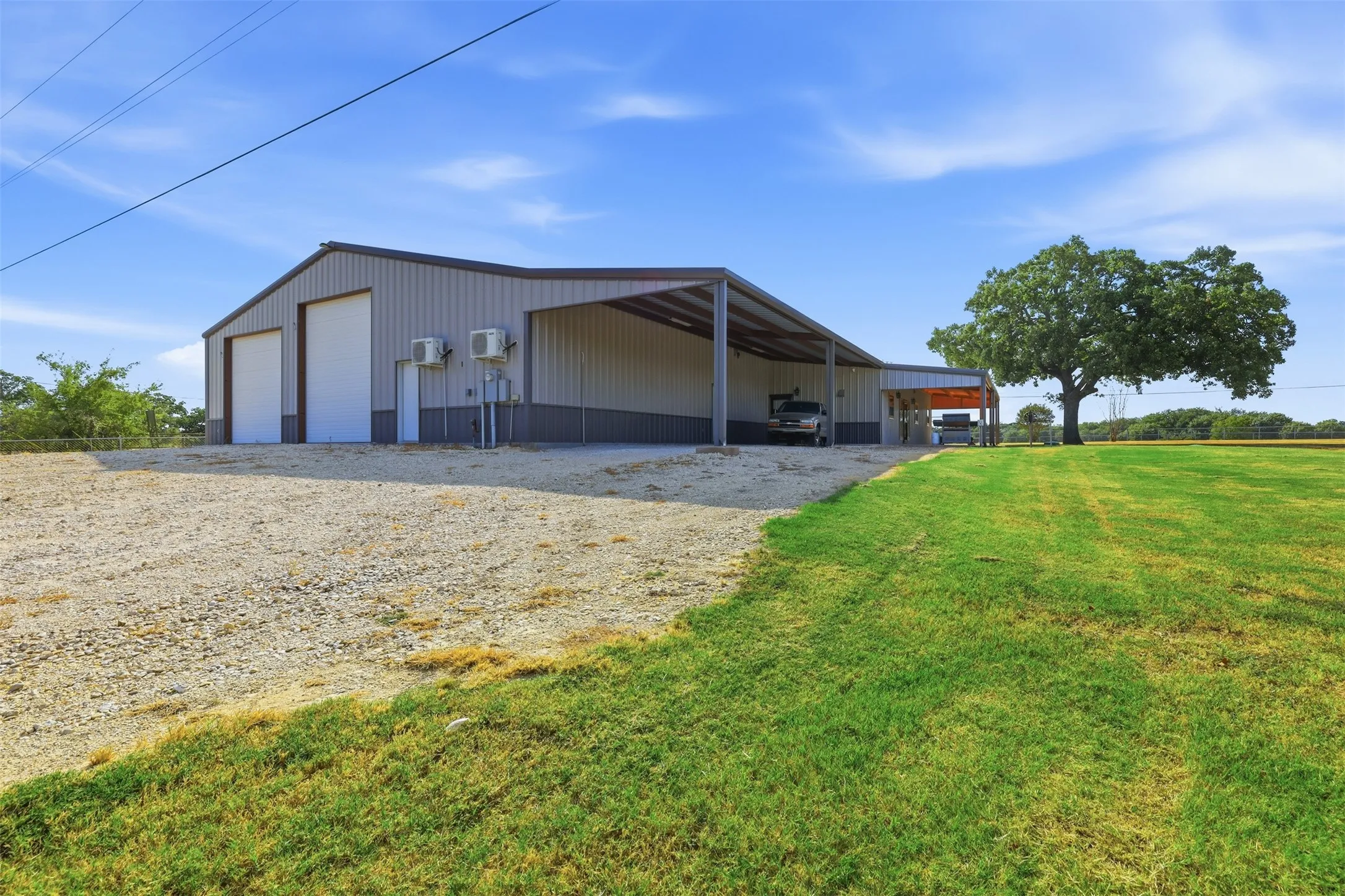 Metal construction building with two large garage doors, an attached covered carport, and gravel driveway