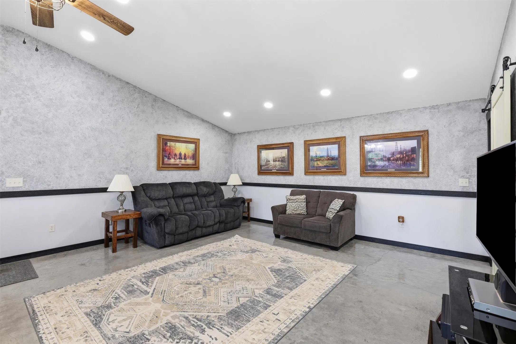 Vaulted ceiling, recessed lighting, ceiling fan, accent wall with wainscoting, and concrete flooring