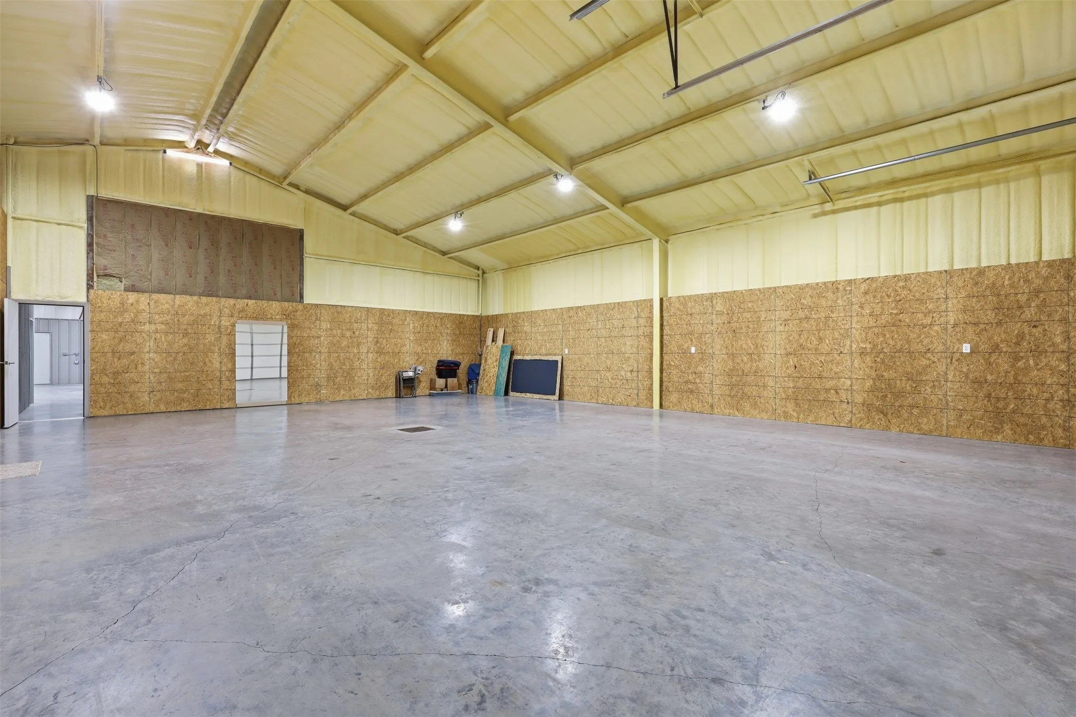 Expansive open space with concrete flooring, high ceilings with exposed beams, and a combination of metal paneling and wood-finish wall treatments