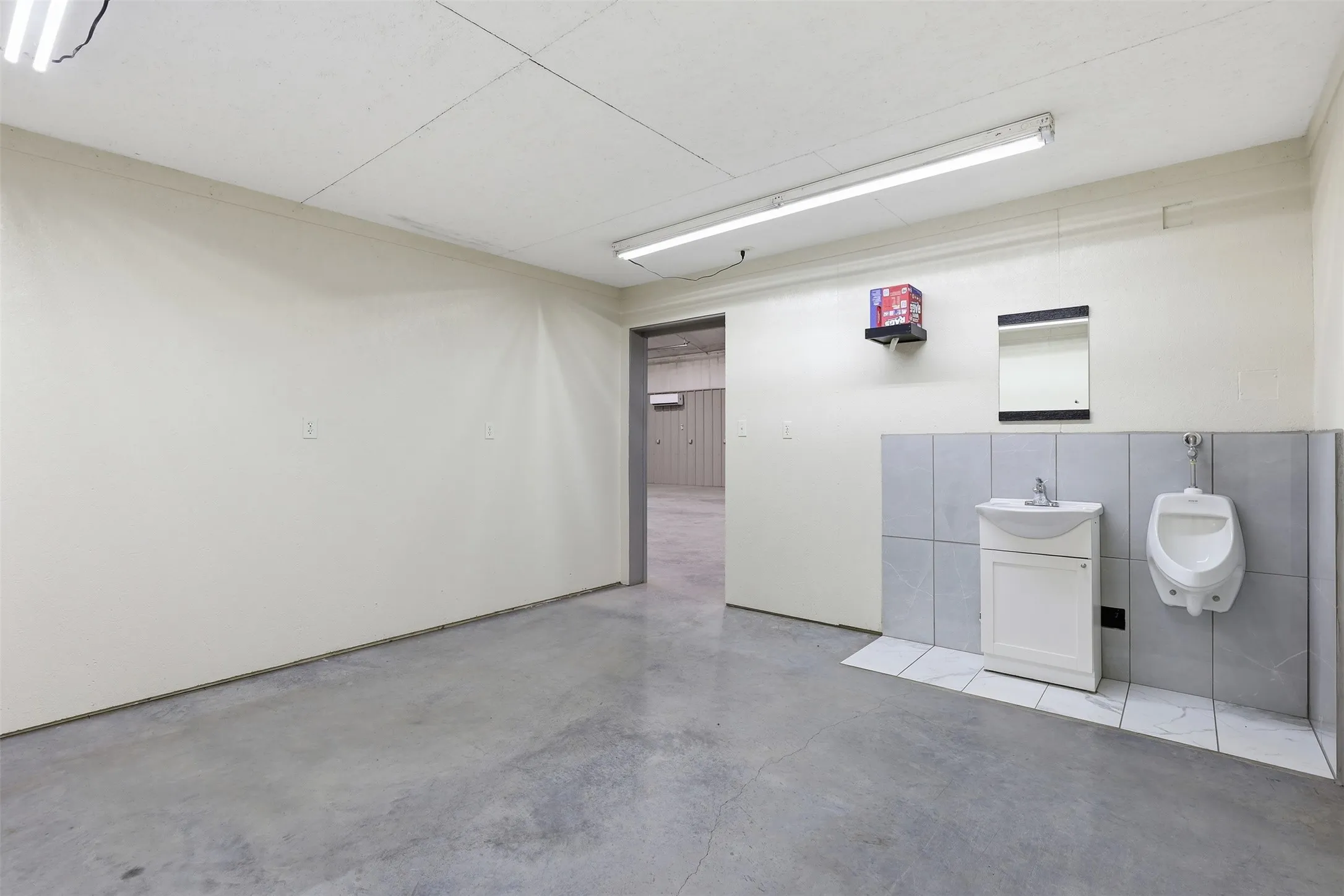 Concrete flooring, drop ceiling, wall-mounted sink vanity, wall-mounted mirror, and tiled walls