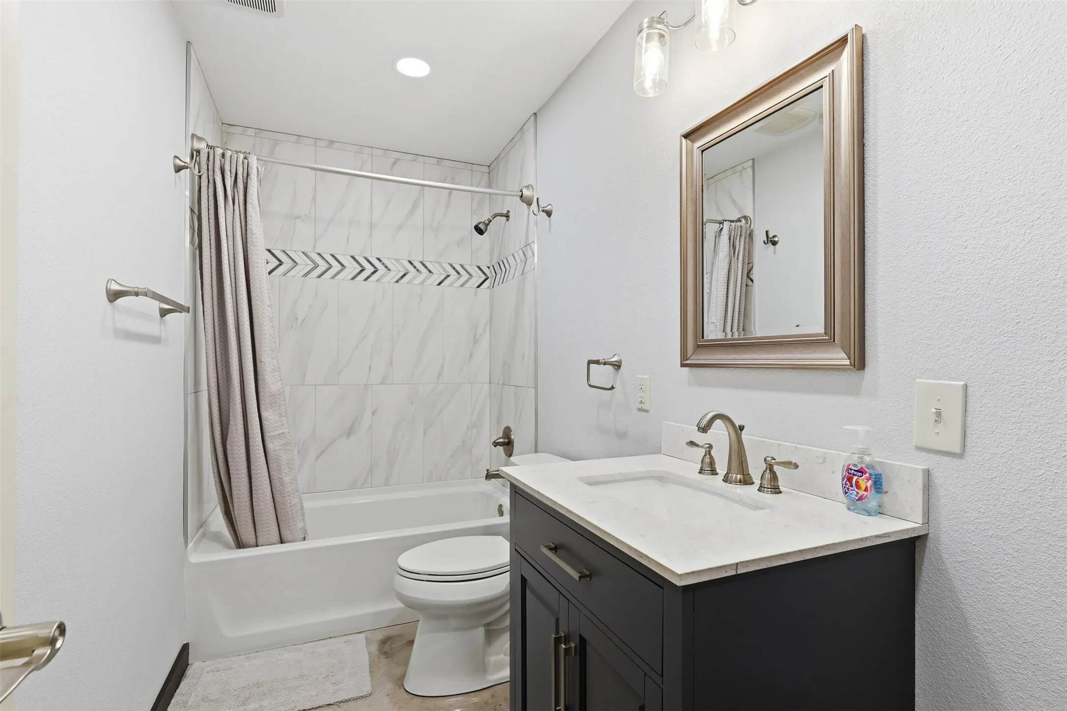 Bathtub with tile surround, vanity with light countertop, framed mirror, and brushed nickel fixtures