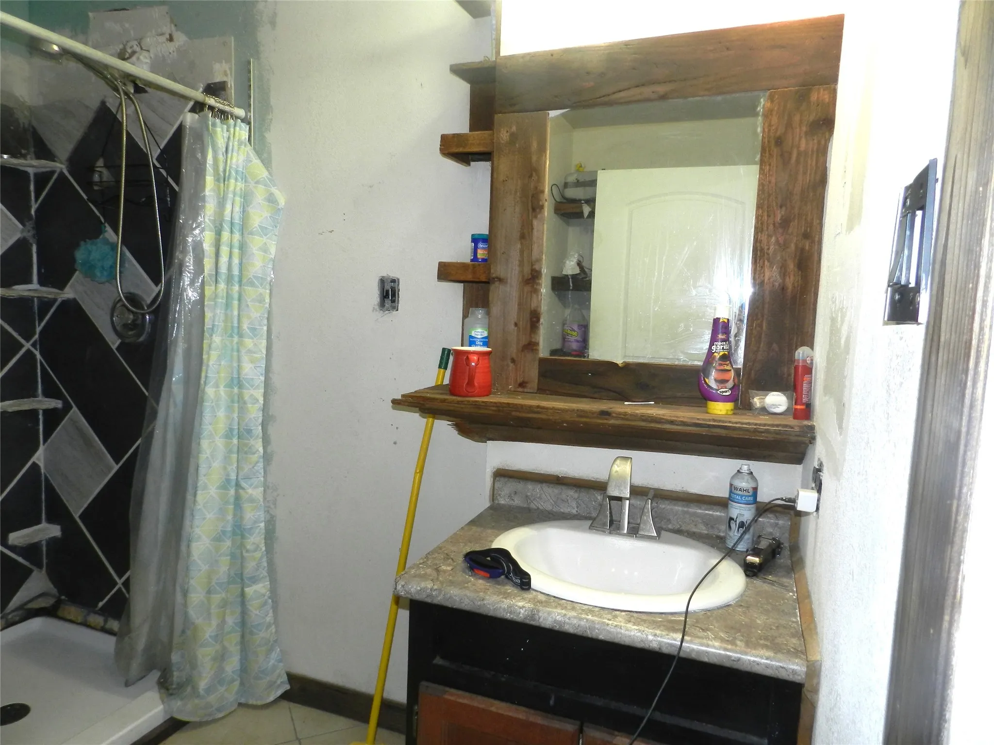 Vanity with a white oval sink, chrome faucet, and a wood-framed mirror with integrated shelving