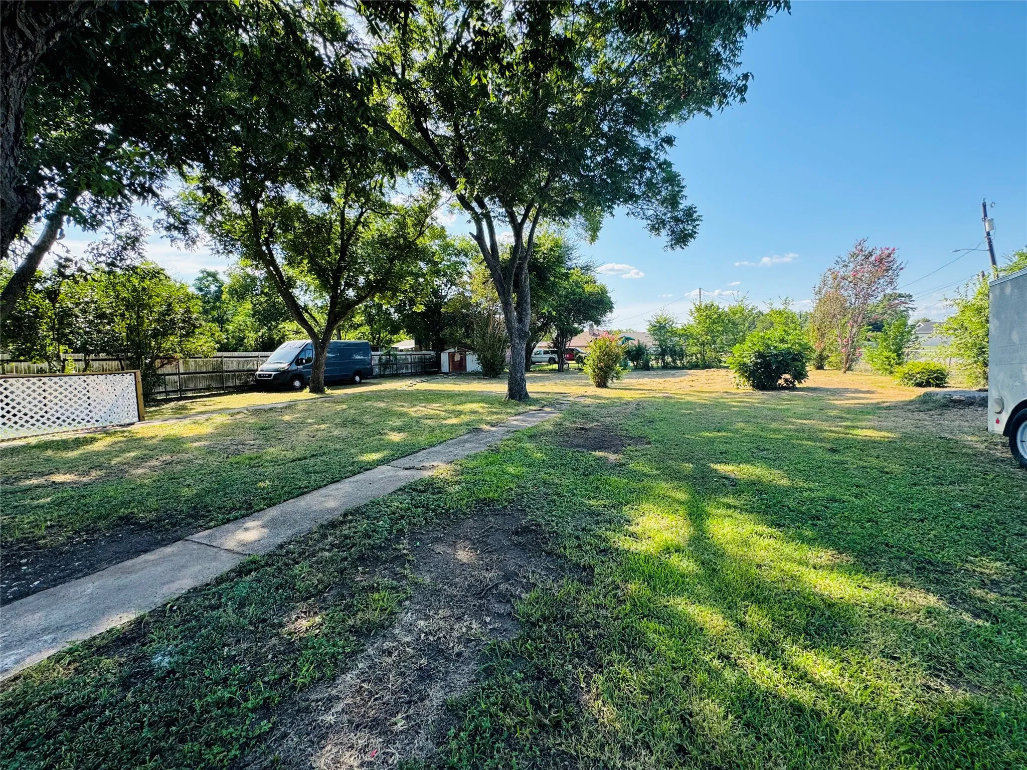 Expansive outdoor space featuring a paved pathway, mature trees, and a wooden privacy fence