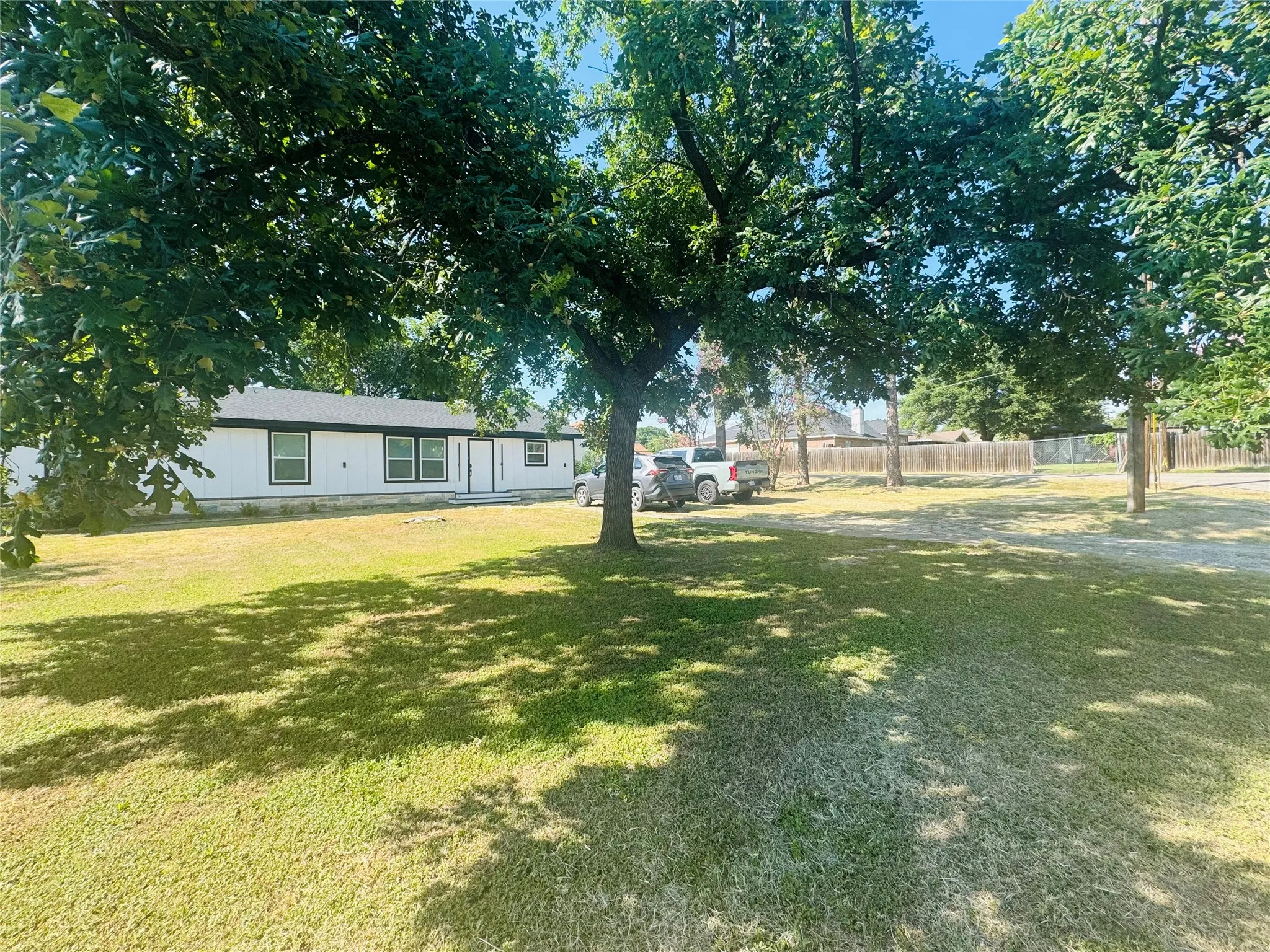 Expansive front yard with mature trees, a white exterior, dark trim, and a fenced perimeter