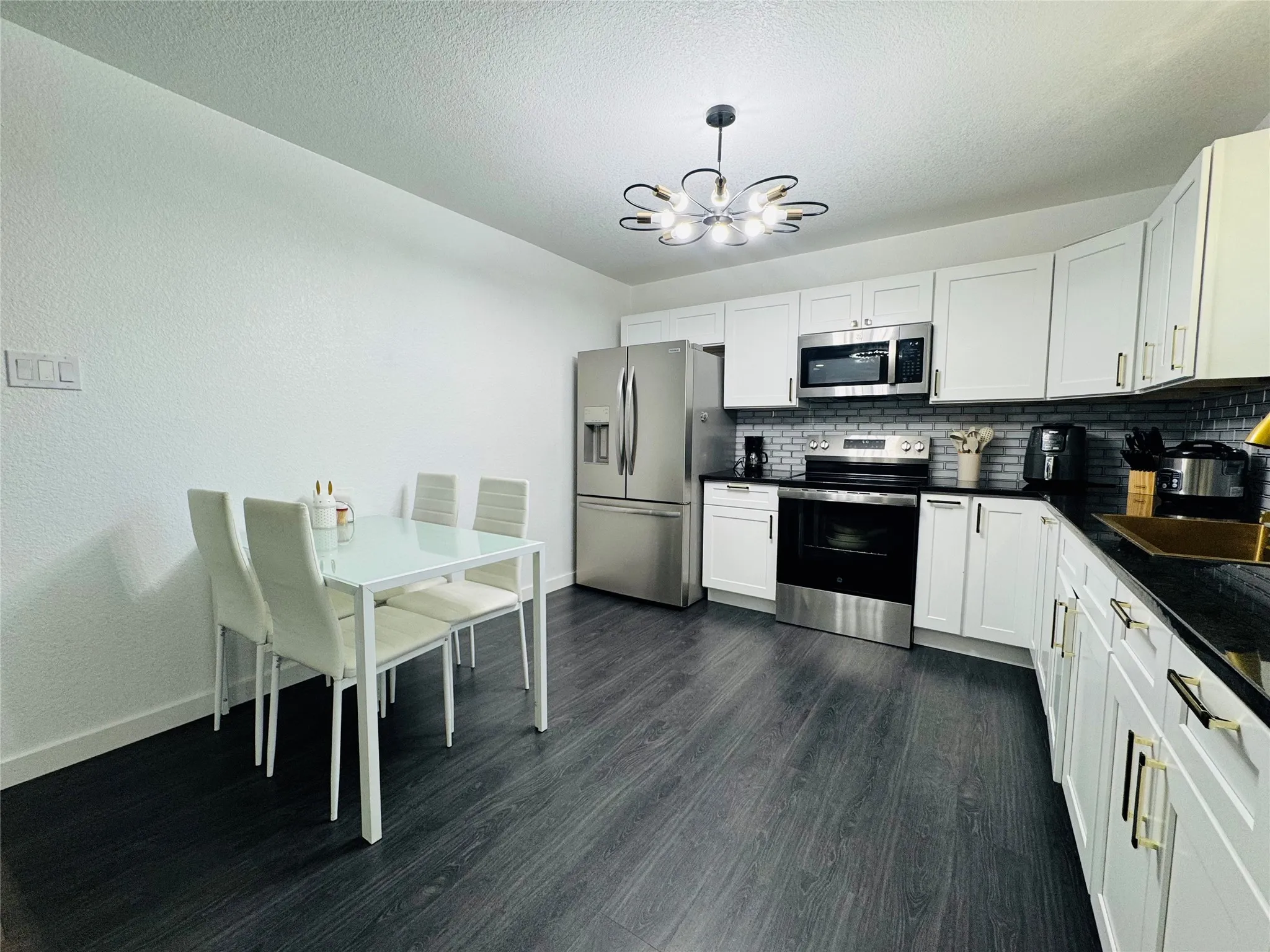 Kitchen featuring white cabinetry, dark countertops, stainless steel appliances, a subway tile backsplash, and dark wood-finish flooring