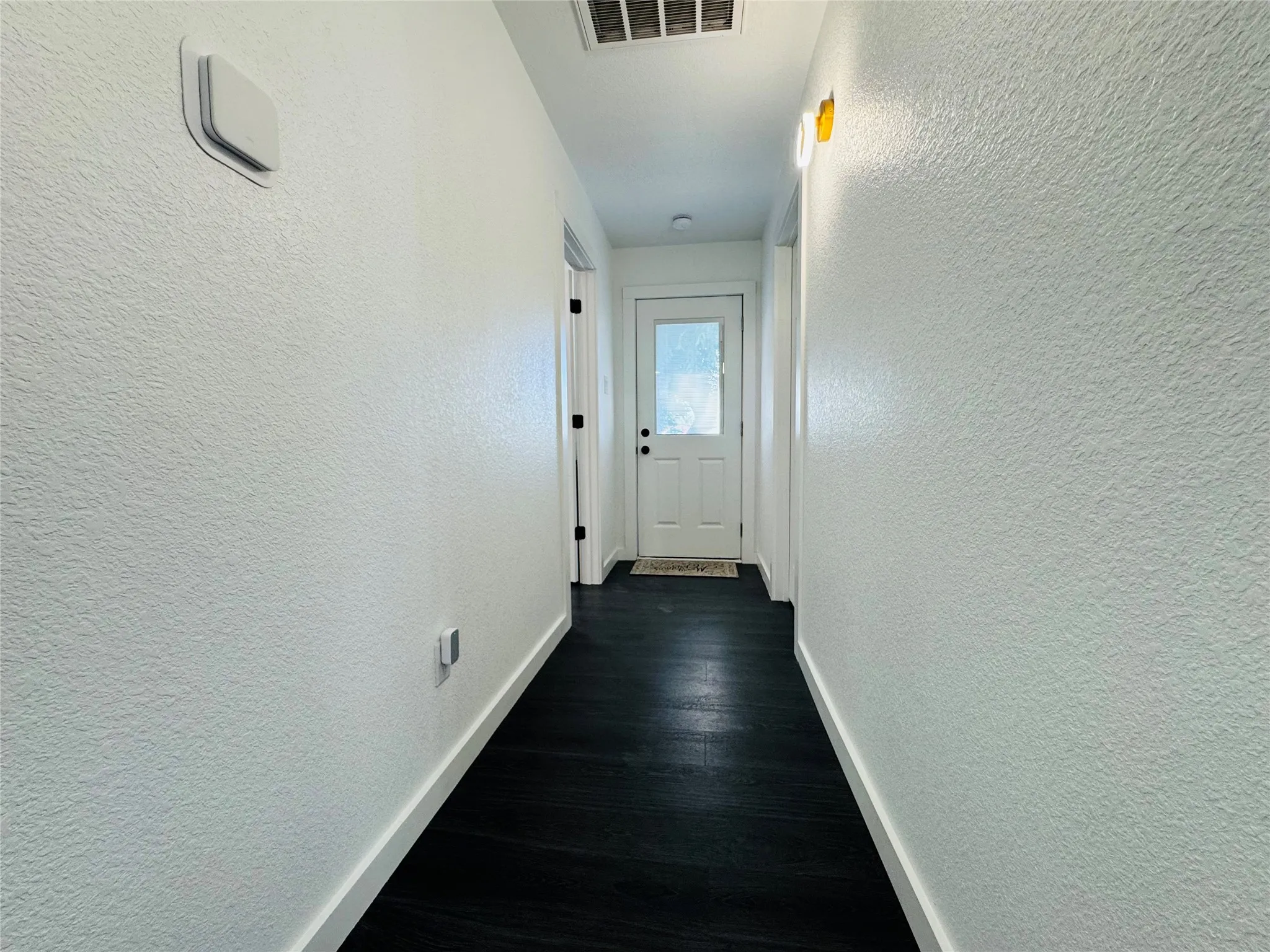 Dark wood-finish flooring with white baseboards and textured walls