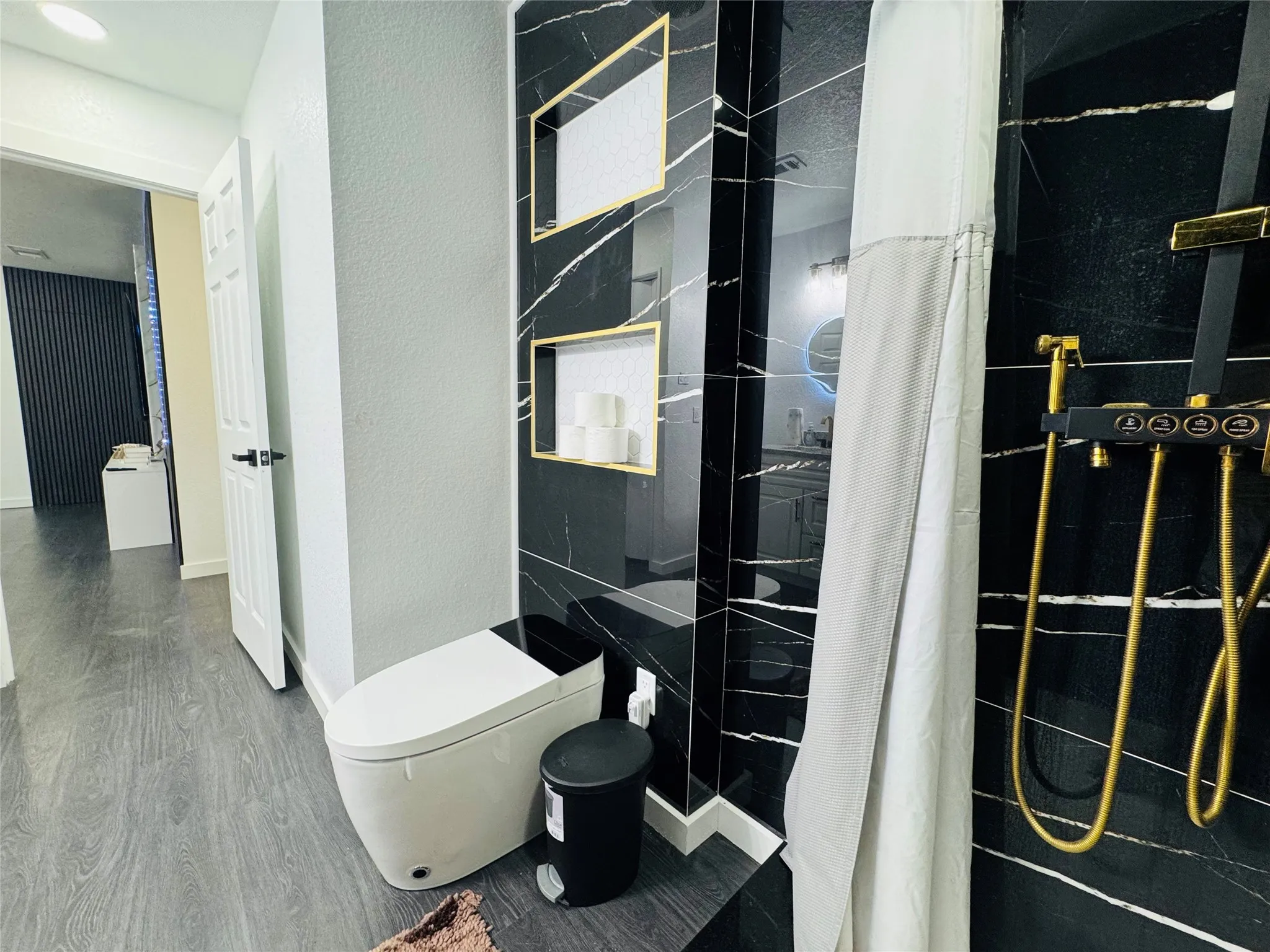 Black marbled wall tiling, gold-tone shower fixtures, built-in shelving with gold-tone accents, and a modern toilet