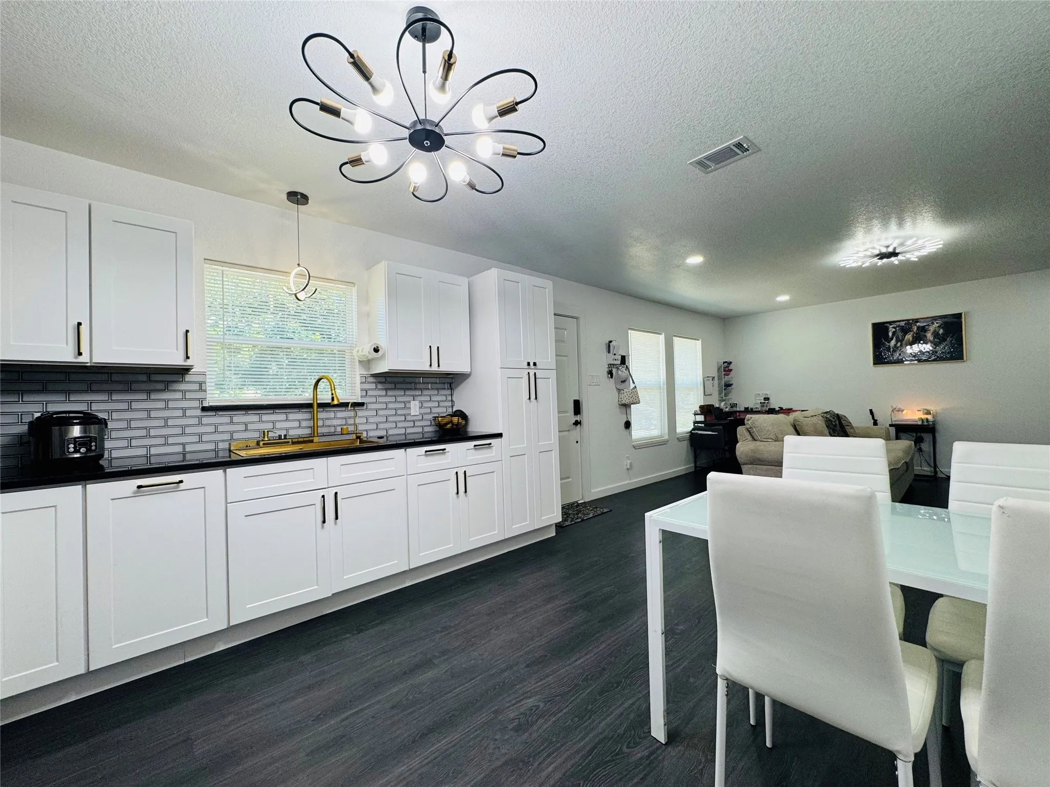 White cabinetry, dark countertops, a subway tile backsplash, wood-finish flooring, and a modern chandelier