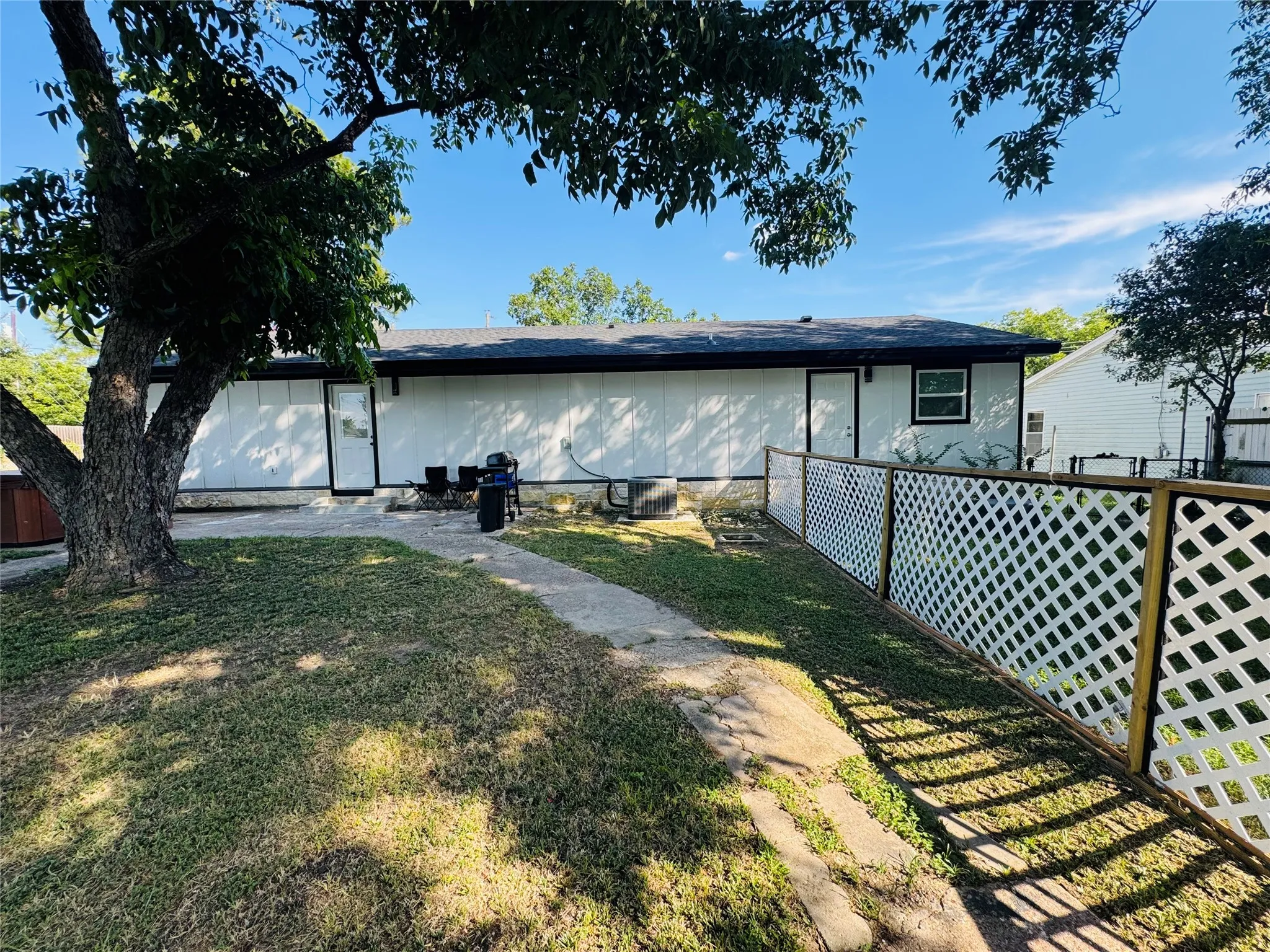 Rear exterior with white siding, a black roof, and a white lattice fence