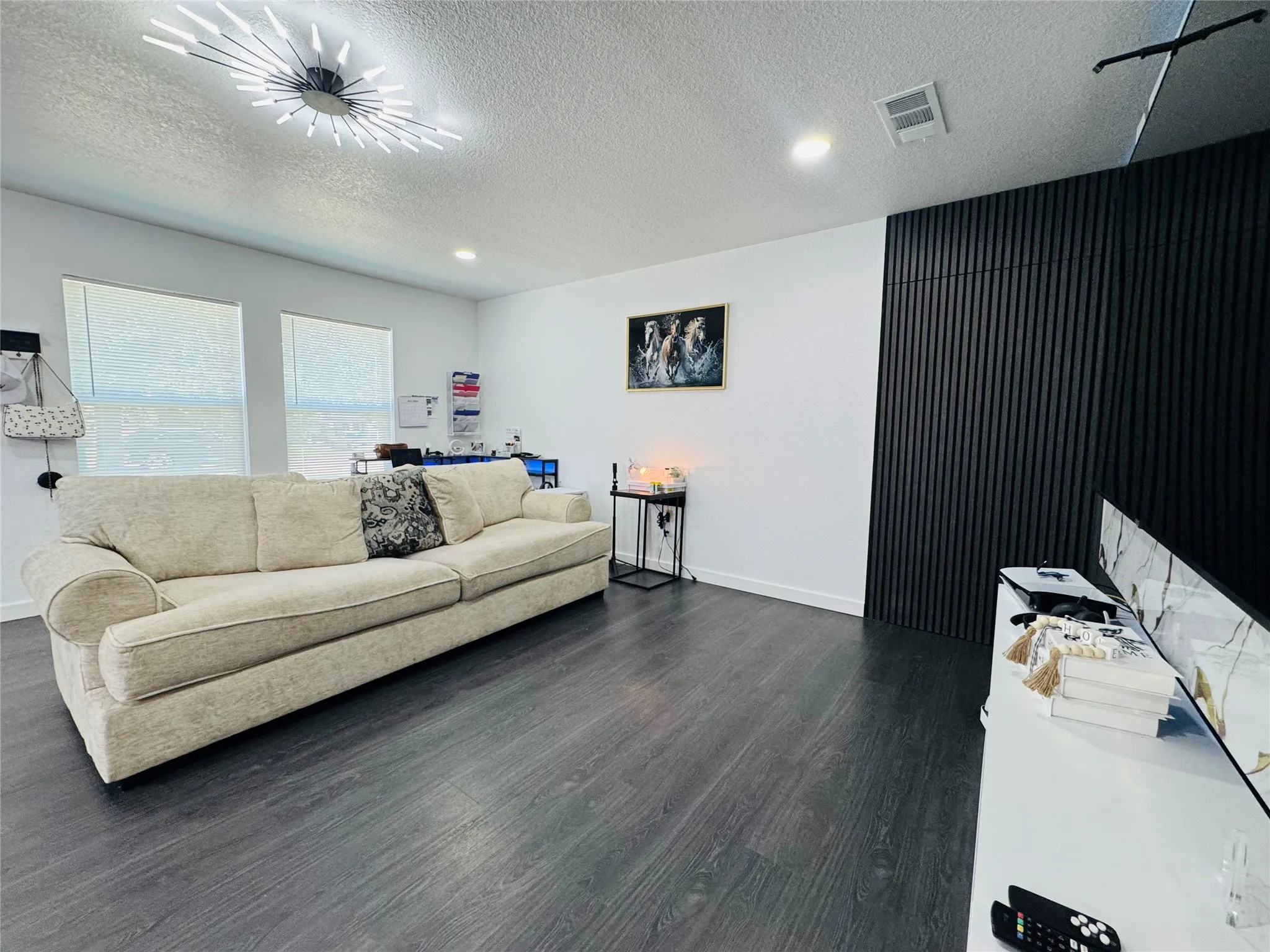 Recessed lighting, wood-finish flooring, accent wall with vertical paneling, and a contemporary ceiling light fixture