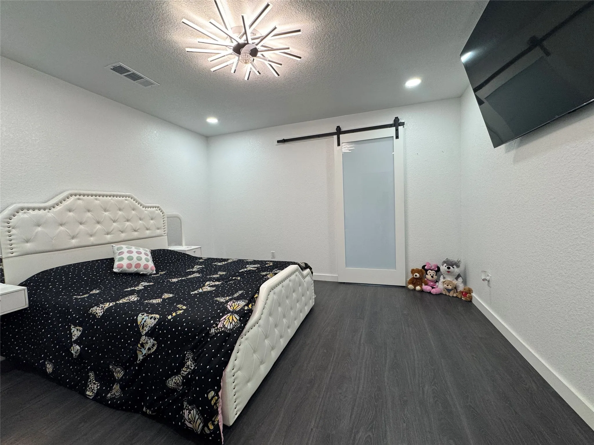 Wood-finish flooring, recessed lighting, modern ceiling fixture, textured walls, and a sliding barn door with frosted glass
