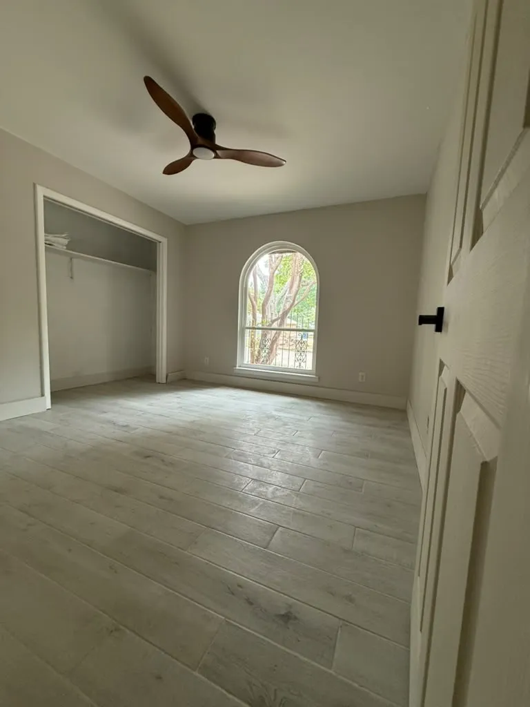 Wood-finish flooring, arched window, modern ceiling fan, and a built-in closet