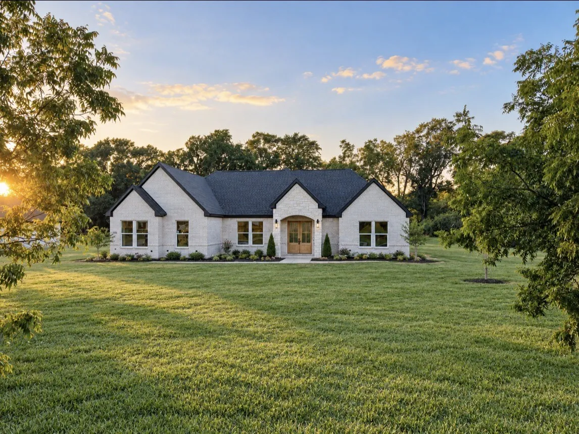 White brick exterior with a dark shingle roof, arched entry, and a light wood-finish double door