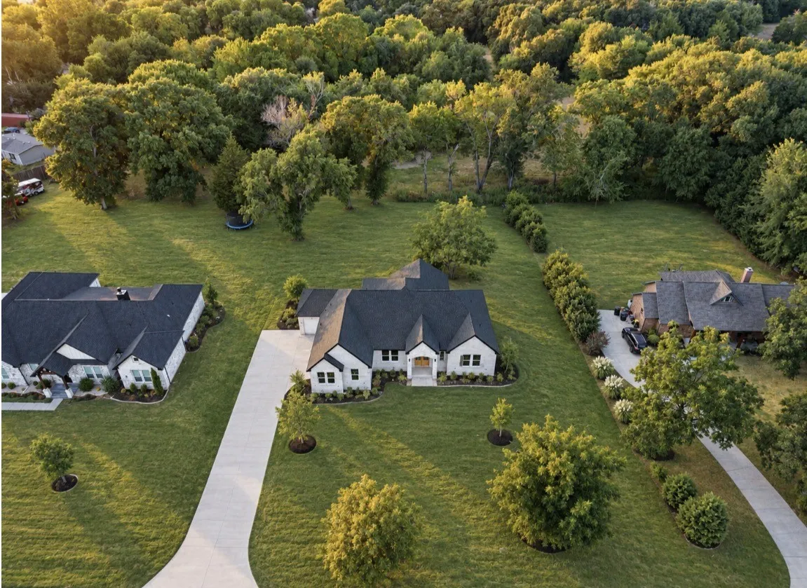 Expansive property featuring a contemporary residence with a dark roof and light-colored exterior, an extended driveway, and mature trees