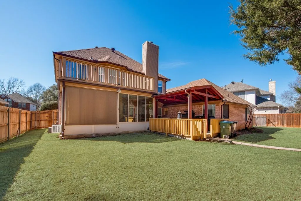 Rear view of property with a balcony, a fenced backyard, a chimney, a yard, and brick siding