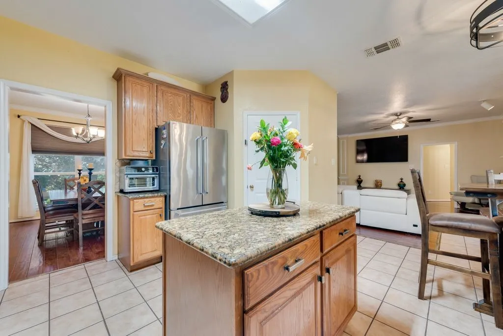 Kitchen featuring light tile patterned floors, ceiling fan with notable chandelier, visible vents, high end fridge, and a center island