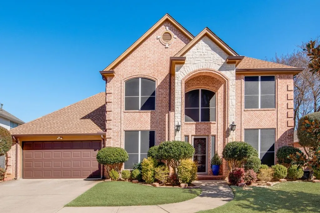 View of front of house with an attached garage, brick siding, a shingled roof, driveway, and stone siding