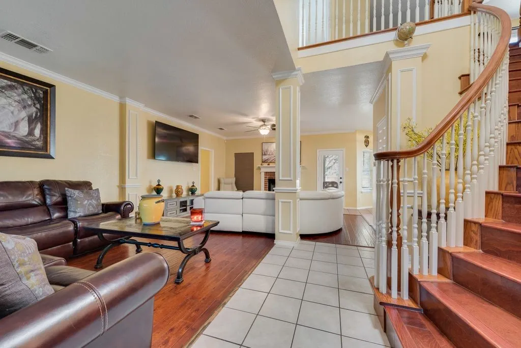 Living room featuring decorative columns, visible vents, ceiling fan, stairway, and crown molding