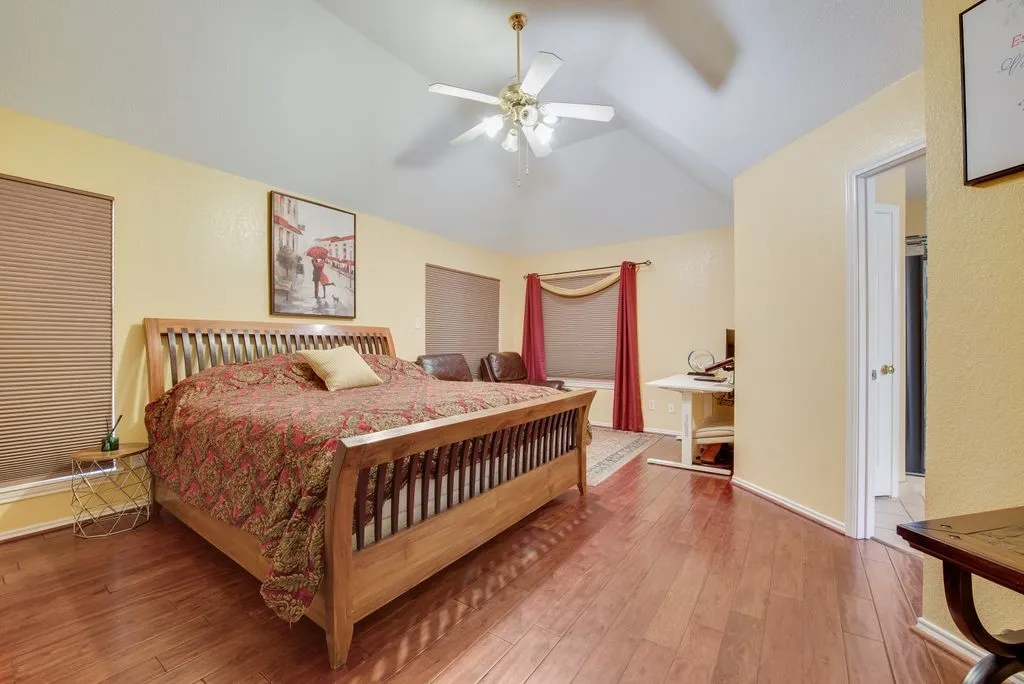 Bedroom featuring lofted ceiling, wood-type flooring, baseboards, and a ceiling fan