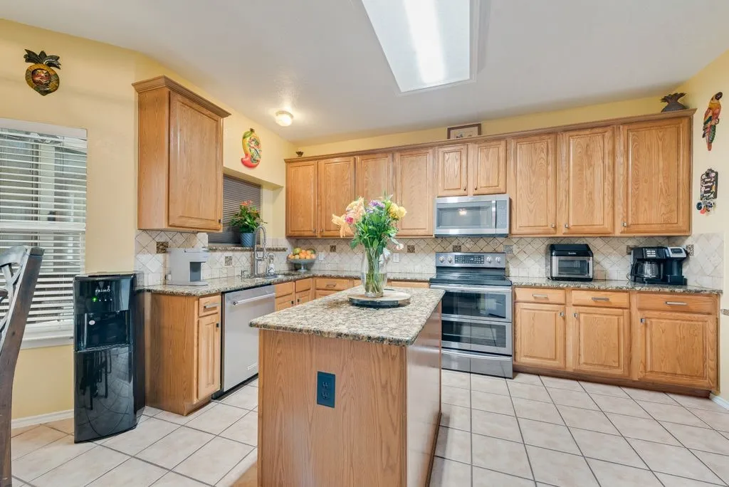 Kitchen featuring light tile patterned floors, decorative backsplash, appliances with stainless steel finishes, light stone counters, and a center island