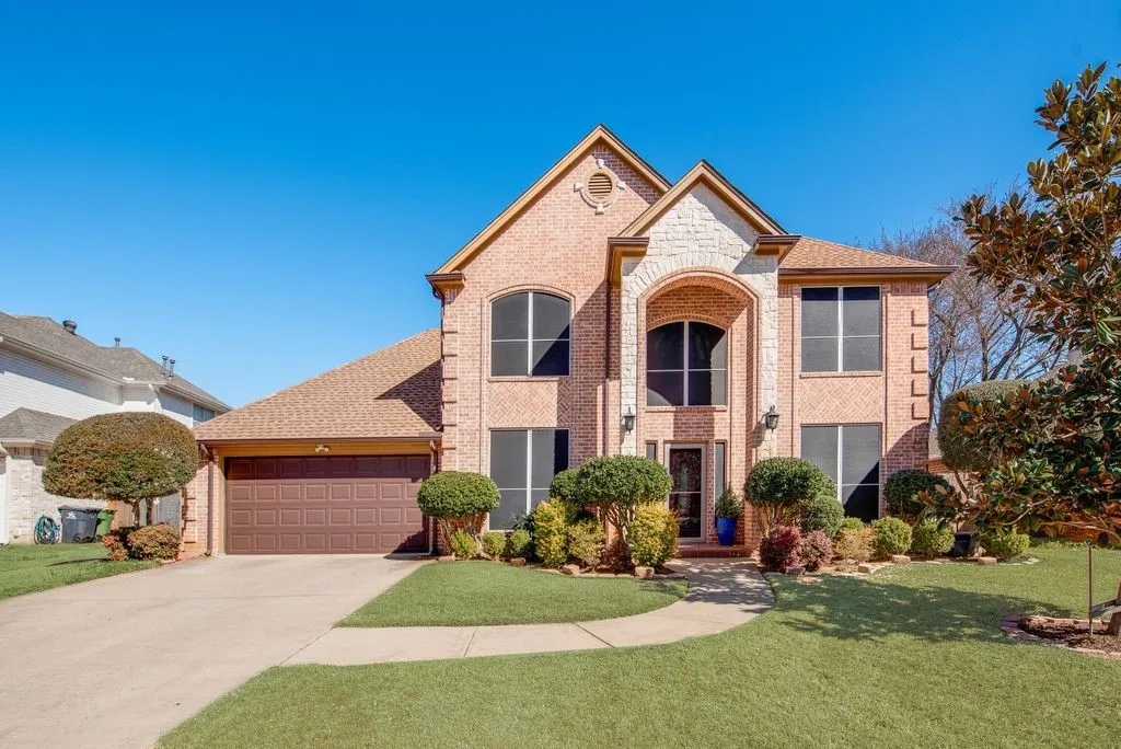 View of front of house with brick siding, roof with shingles, concrete driveway, a garage, and a front lawn