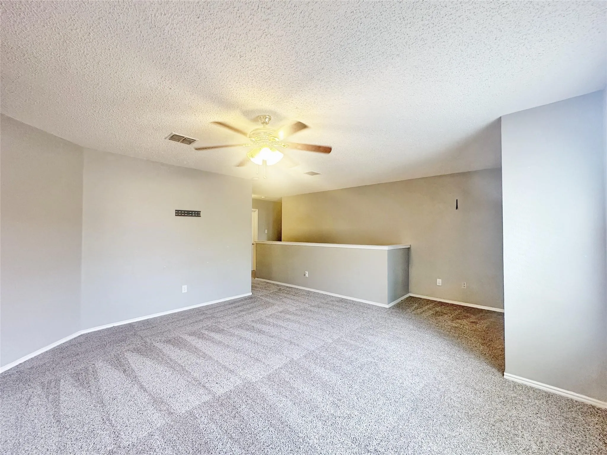 Carpeted flooring, neutral wall tones, partial wall, and ceiling fan