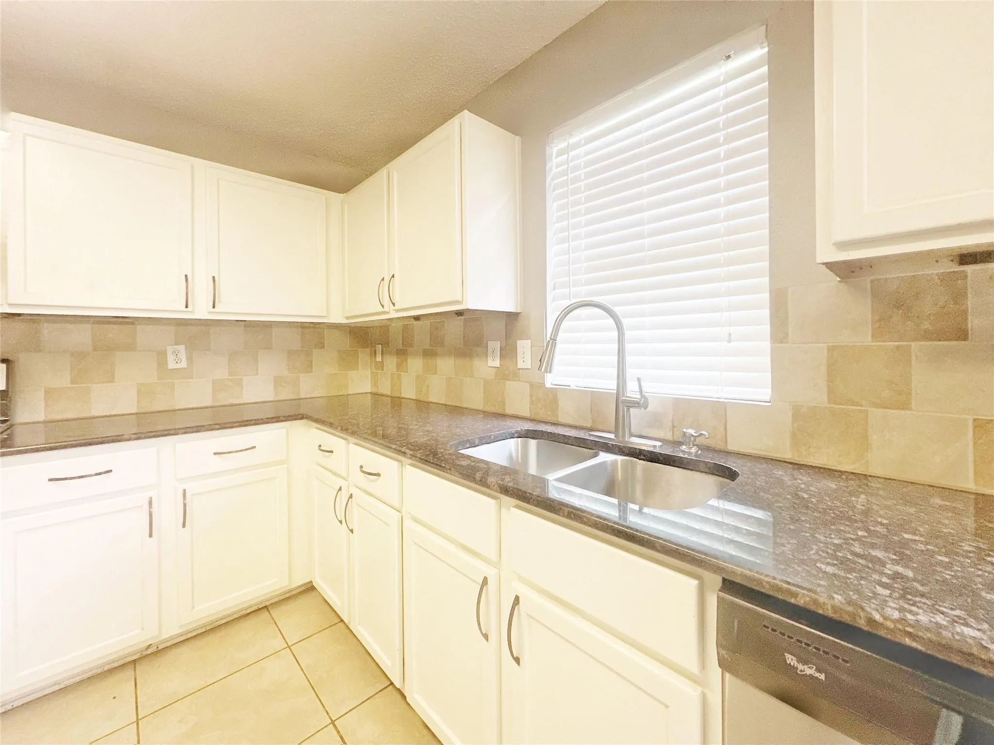 White cabinetry, dark stone countertops, tile backsplash, stainless steel double basin sink, and tile flooring