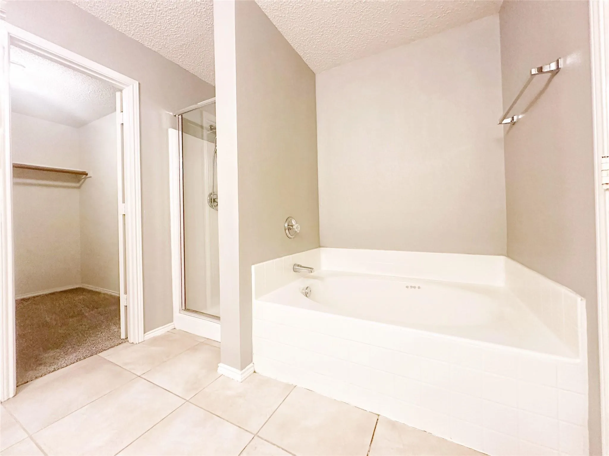 Tiled flooring, corner soaking tub, glass-enclosed shower, and a walk-in closet with shelving and hanging rod