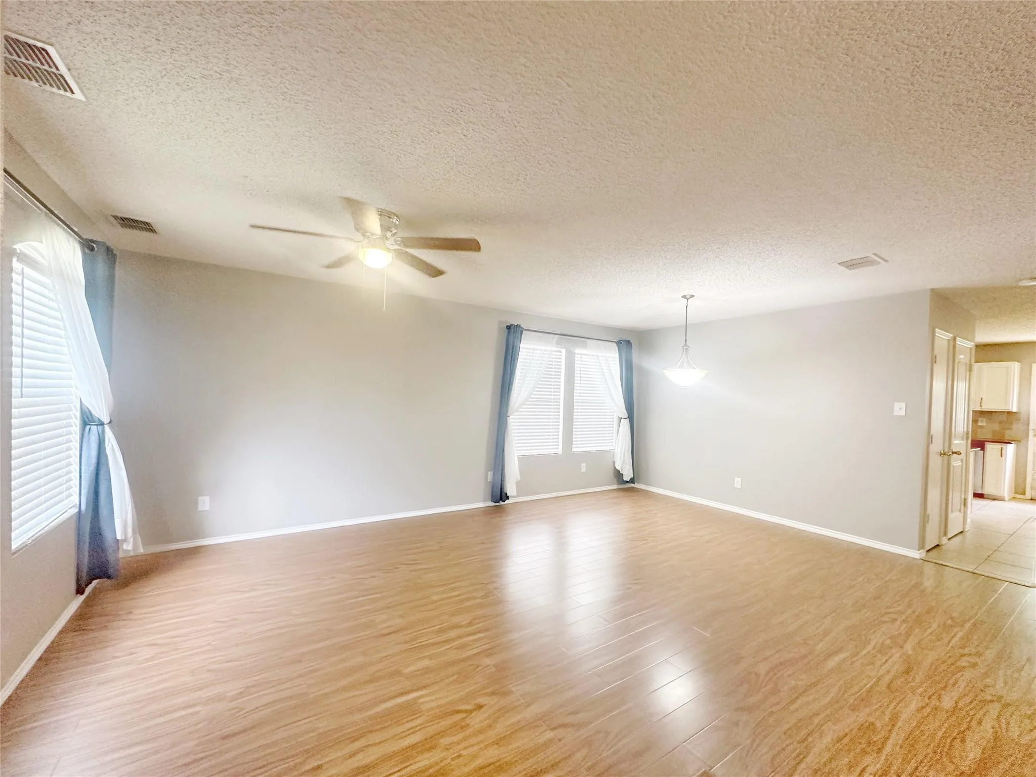 Expansive room featuring wood-finish flooring, multiple windows with blinds, a ceiling fan, and a suspended lighting fixture