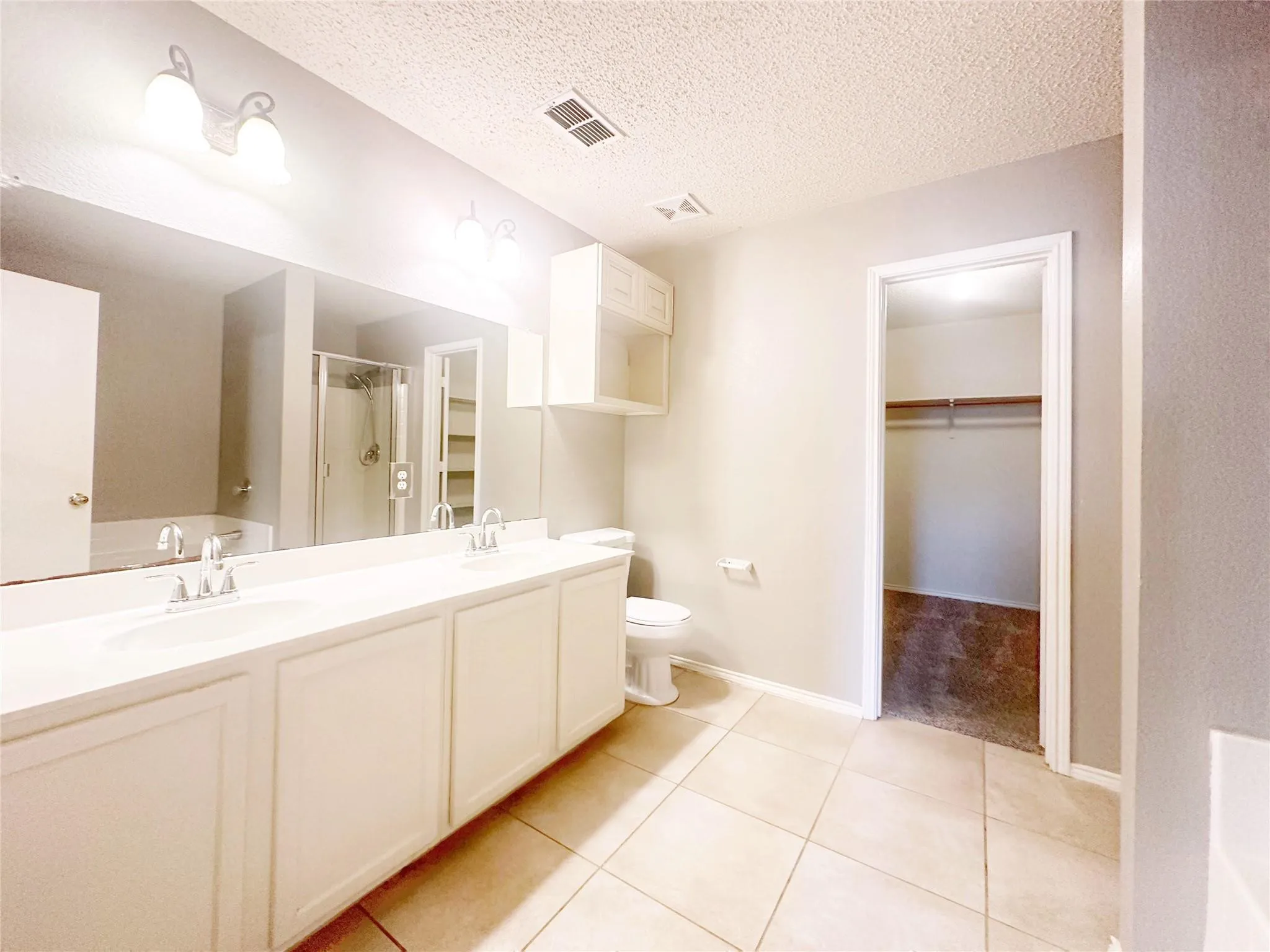 Dual vanity with integrated sinks, framed mirror, built-in upper cabinetry, tile flooring, and walk-in closet with hanging rod