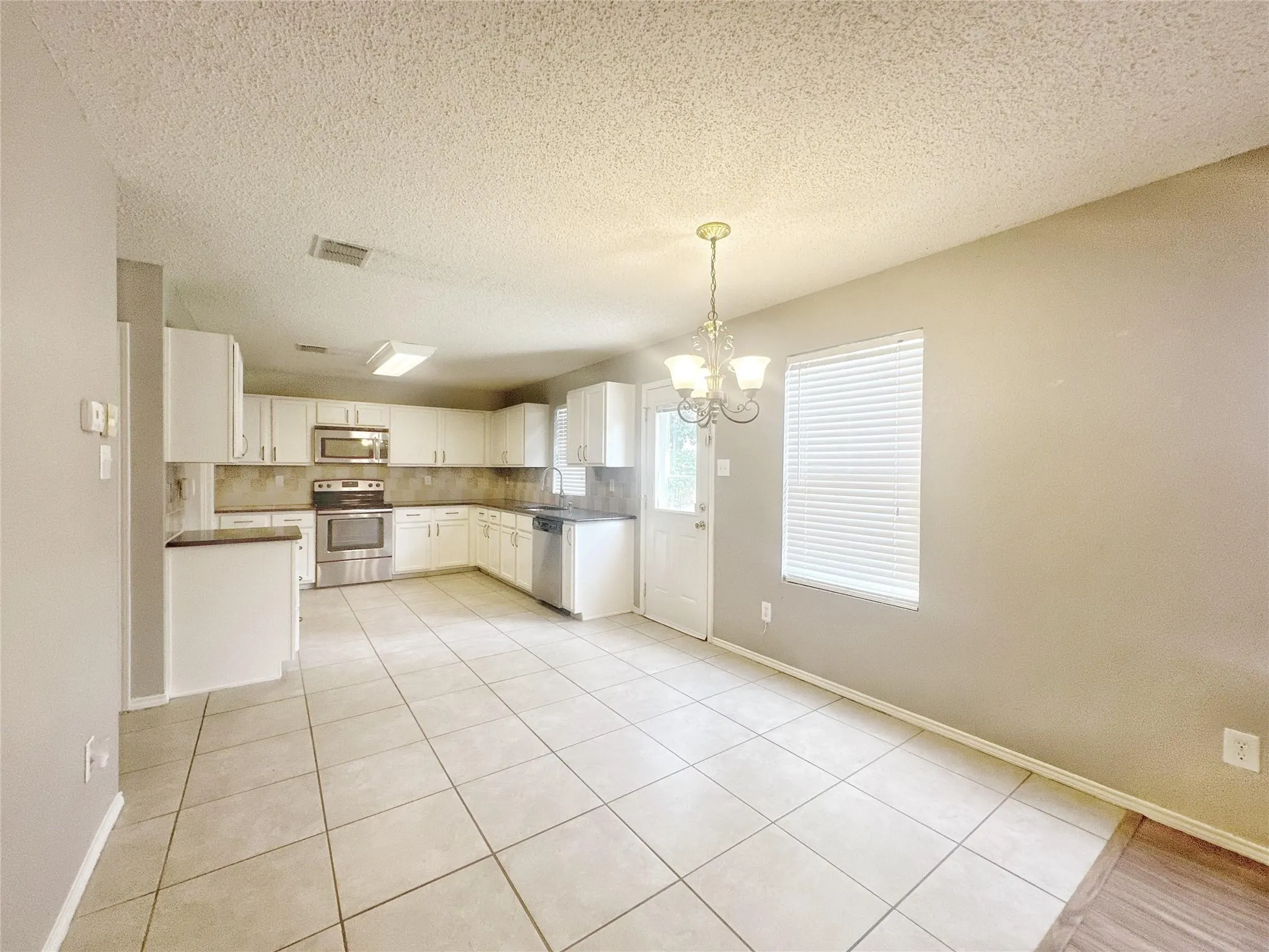 White cabinetry with brushed nickel hardware, stainless steel appliances, tiled backsplash, large format tile flooring, and a dining area with a chandelier