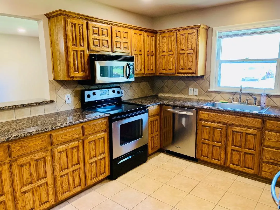 Kitchen featuring wood cabinetry, granite-style countertops, stainless steel appliances, and a tiled backsplash
