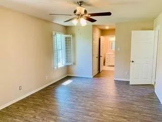 Wood-finish flooring, ceiling fan with integrated lighting, window with plantation shutters, and a white paneled door