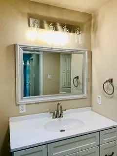 Vanity with white countertop, undermount sink, brushed nickel faucet, and framed mirror with integrated lighting