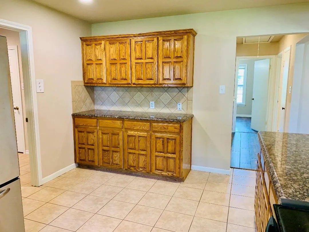 Wood-finish cabinetry with paneled doors, stone-finish countertops, ceramic tile backsplash, and ceramic tile flooring