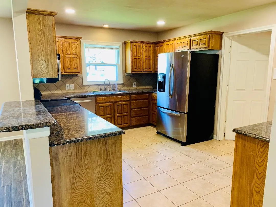 Kitchen featuring wood cabinetry, granite-finish countertops, tiled flooring, and a stainless steel refrigerator