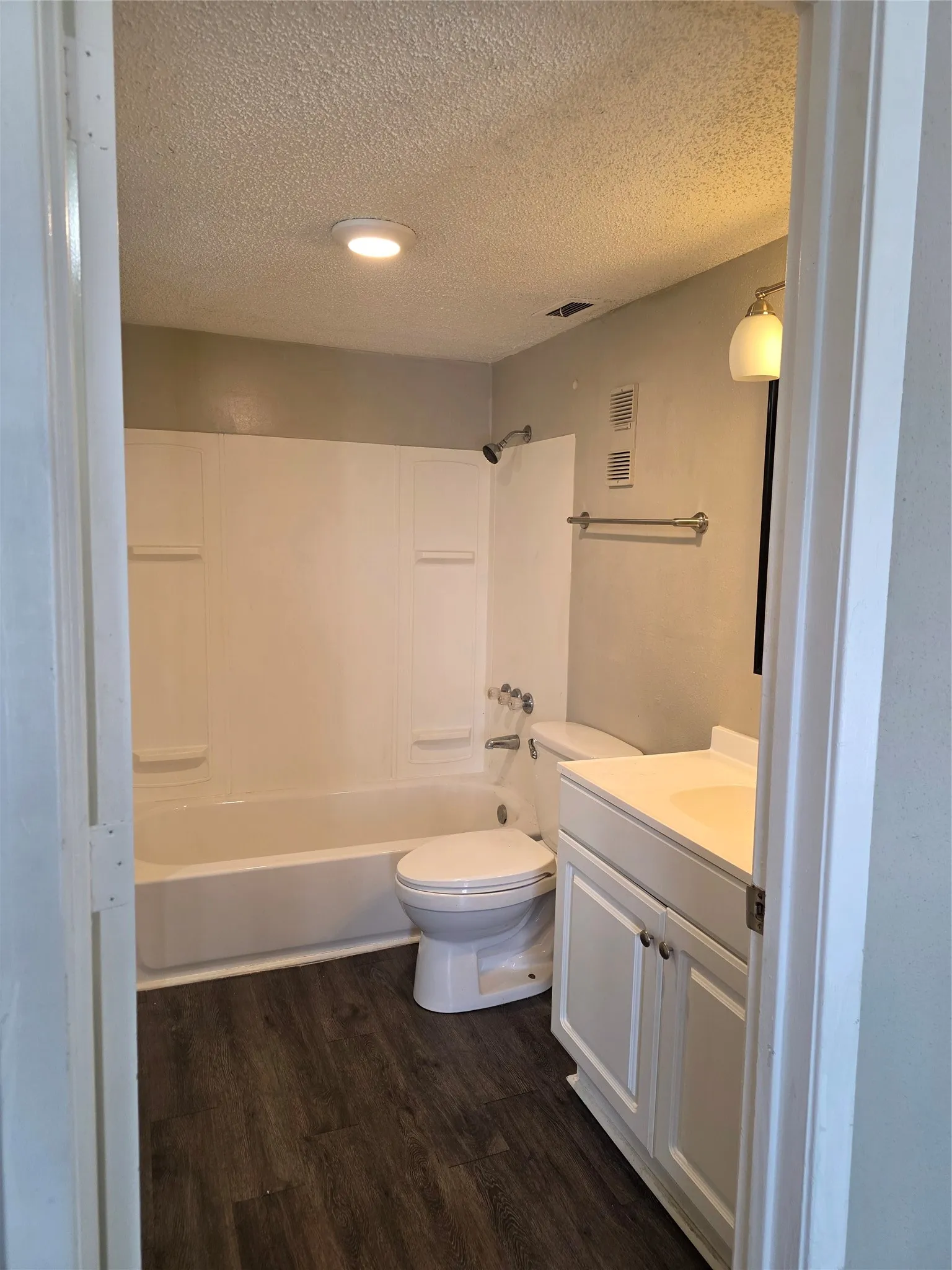 Full bathtub with white surround, wood-finish flooring, white vanity with integrated sink, and recessed ceiling lighting