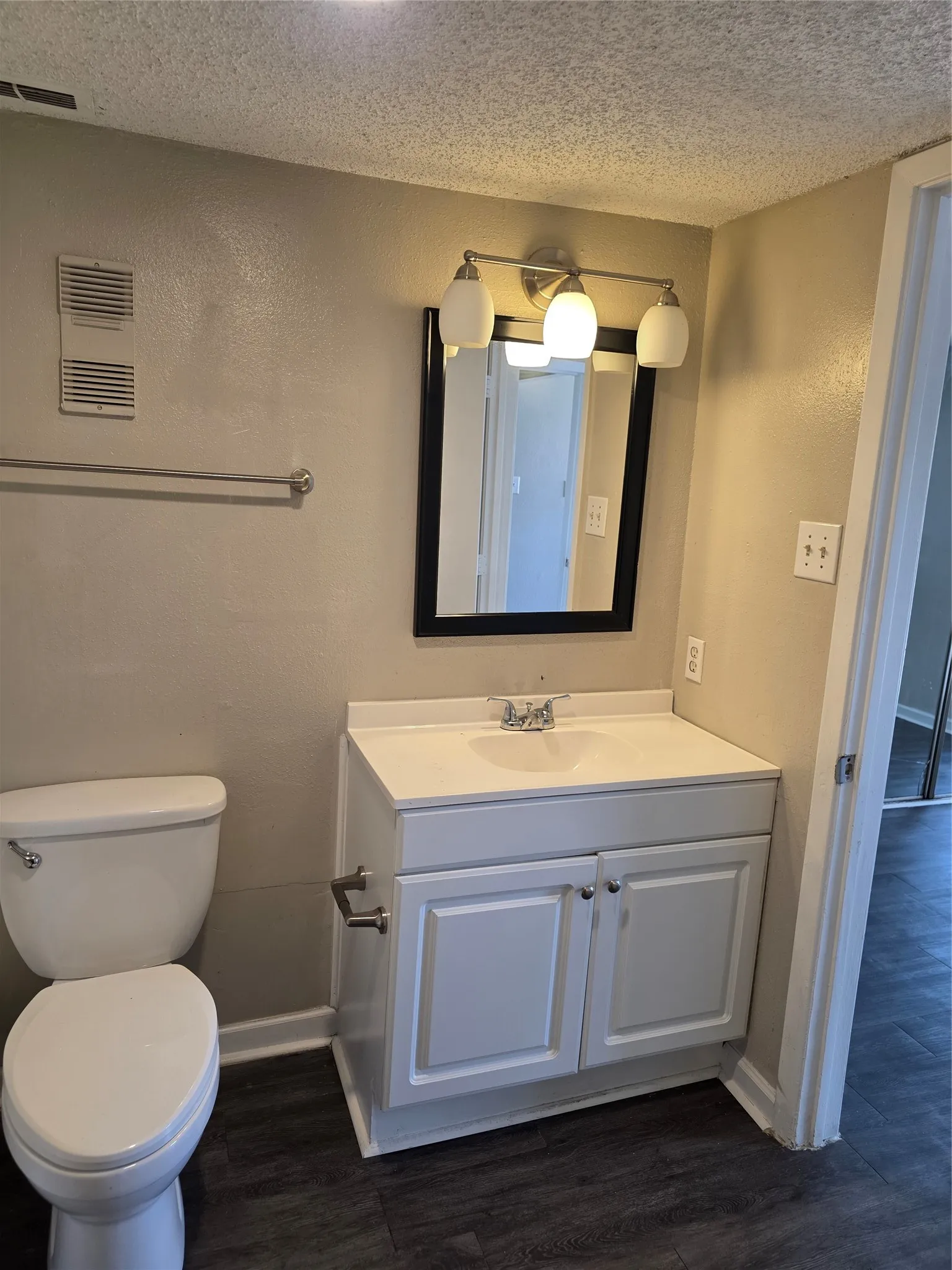 Bathroom featuring a white vanity with integrated sink, panel cabinetry, a framed mirror, and a three-light fixture