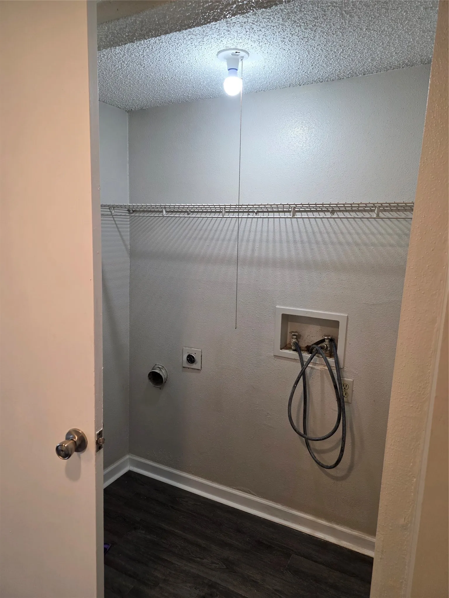 Dedicated laundry area featuring a wire shelf, wall-mounted utility box, and wood-finish flooring