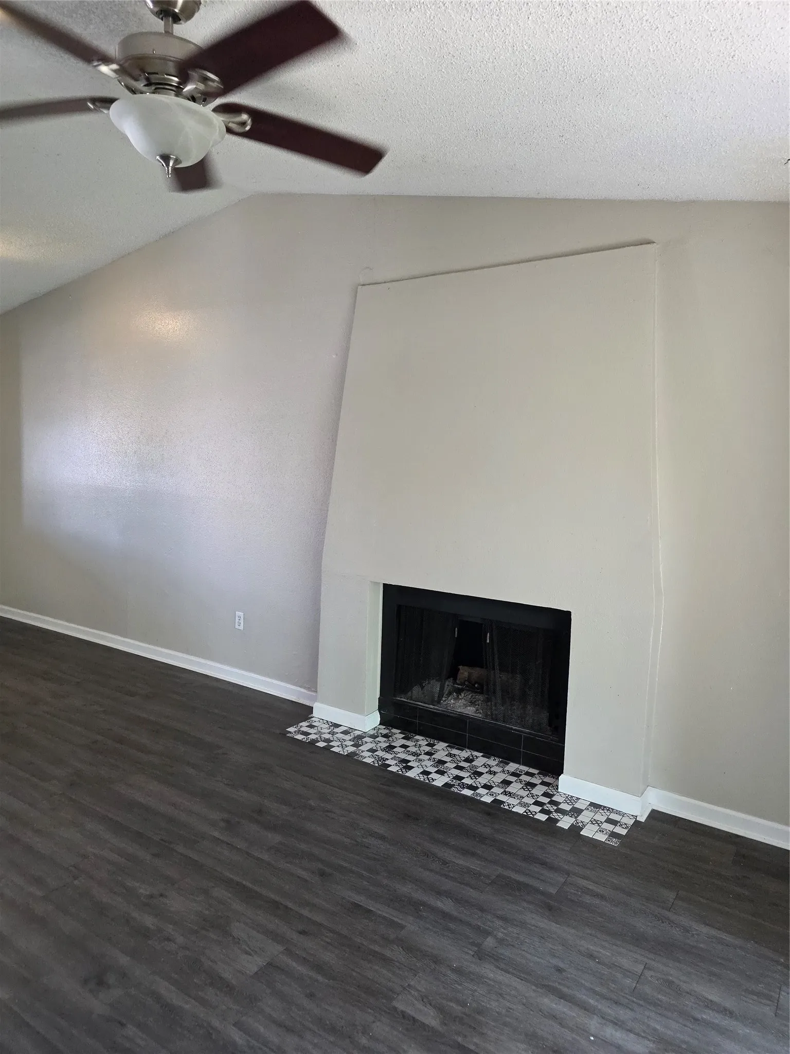 Vaulted ceiling with a ceiling fan, fireplace with a tile hearth, and wood-finish flooring