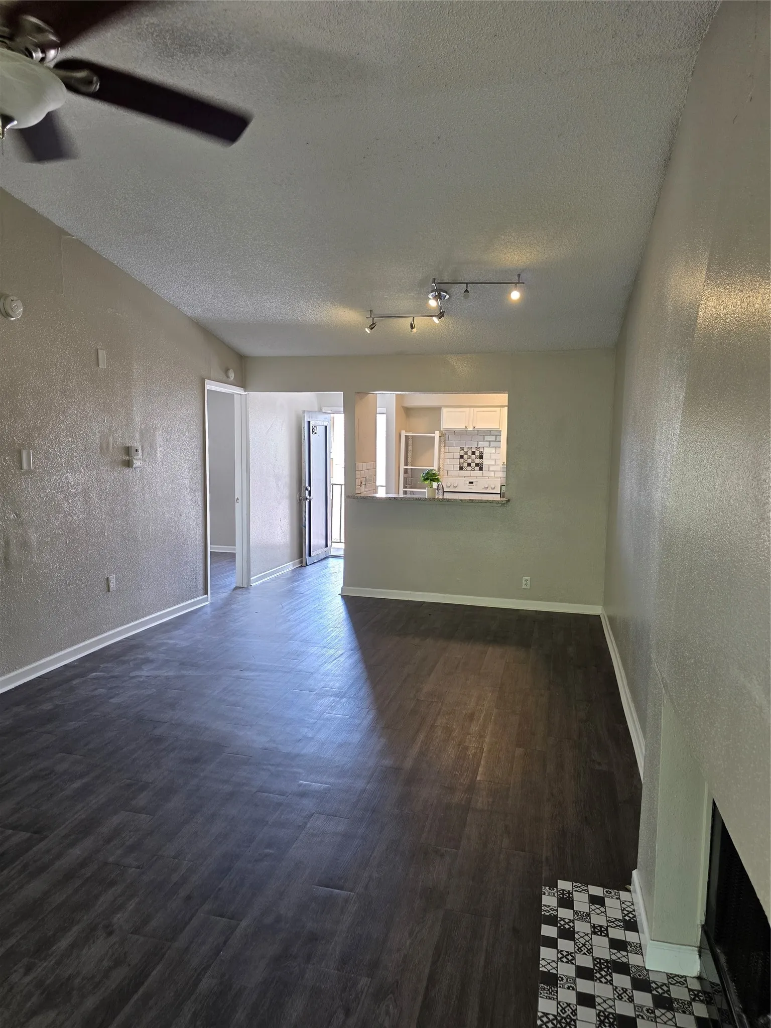 Wood-finish flooring throughout, ceiling fan, track lighting, and a kitchen pass-through with a breakfast bar