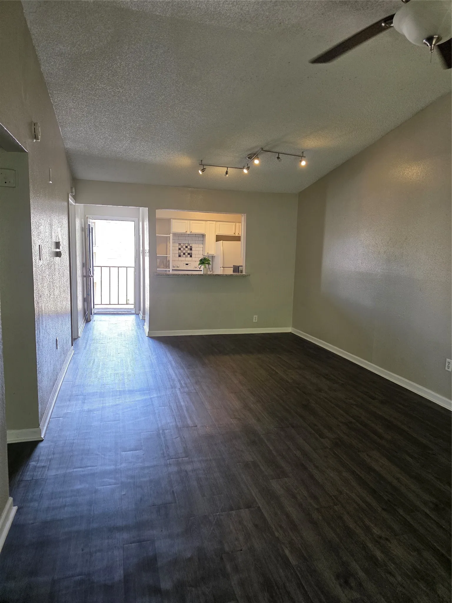 Wood-finish flooring throughout, vaulted ceiling, track lighting, ceiling fan, and a pass-through kitchen window