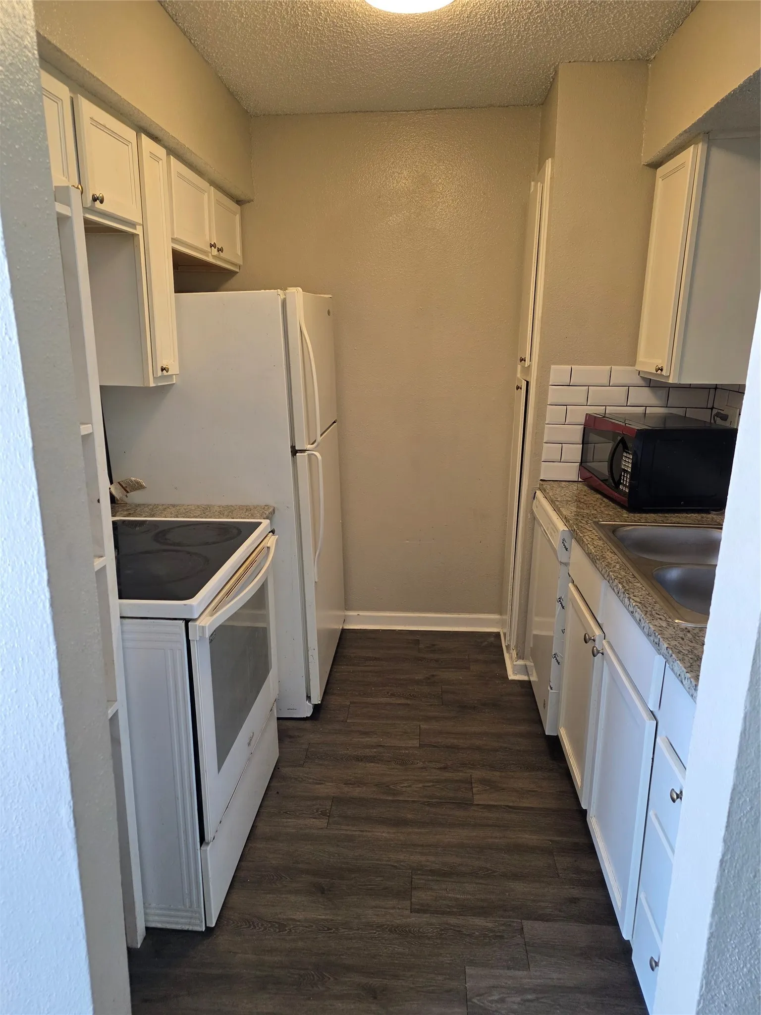 Compact kitchen featuring white cabinetry, white appliances, wood-finish flooring, and subway tile backsplash